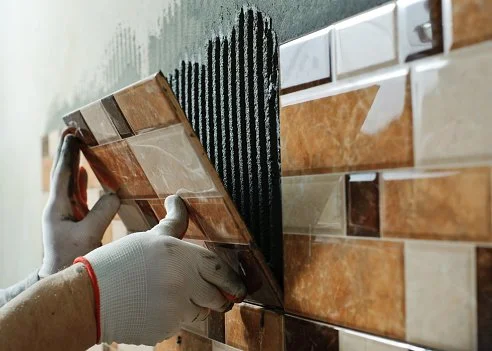 A person installing backsplash tiles on a wall in a kitchen.
