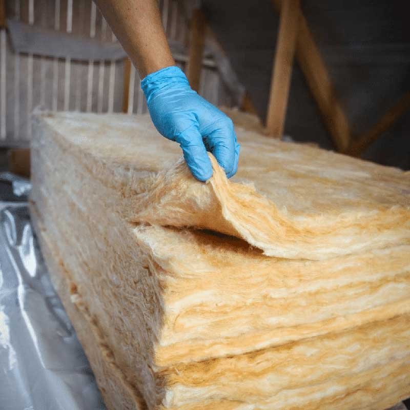 A person installing insulation material from a large wooden beam.