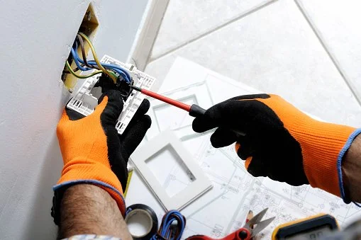 A person working on electrical wires using a screwdriver in an outlet box.