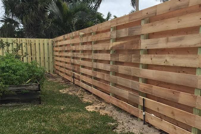 New wooden fence under construction with finished fence on the left and ongoing build on the right, in a backyard with grass and trees.