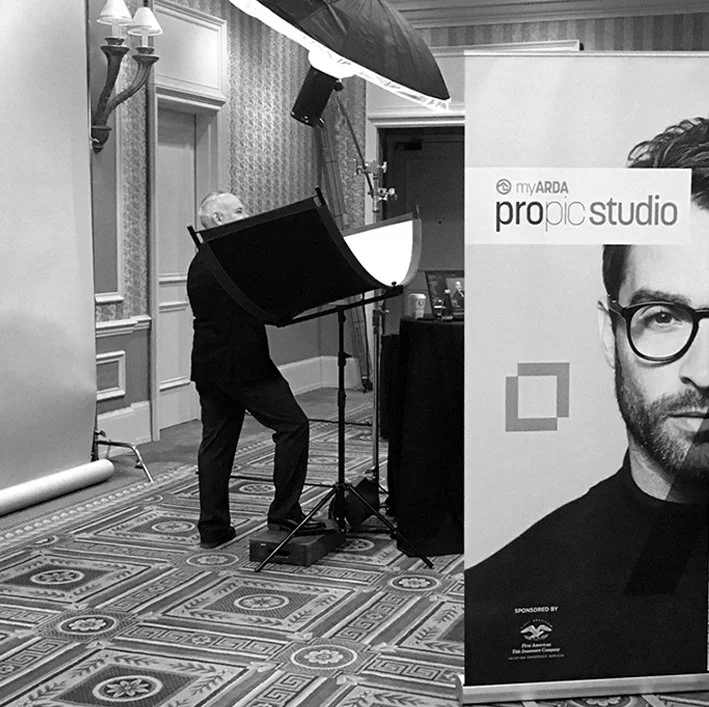 Photographer setting up lighting equipment at a studio with a large portrait banner for 'propic studio' in the foreground.