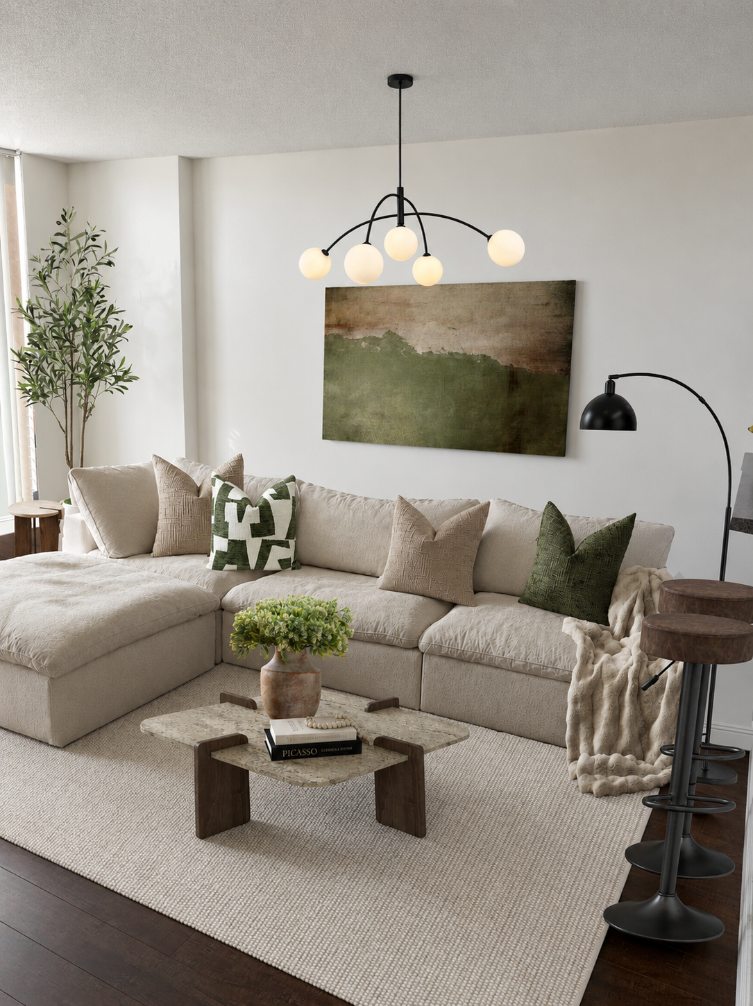 Living room with a beige sectional sofa, decorative pillows, a wall art, a floor lamp, a coffee table with books and a plant, and greenery in the corner.