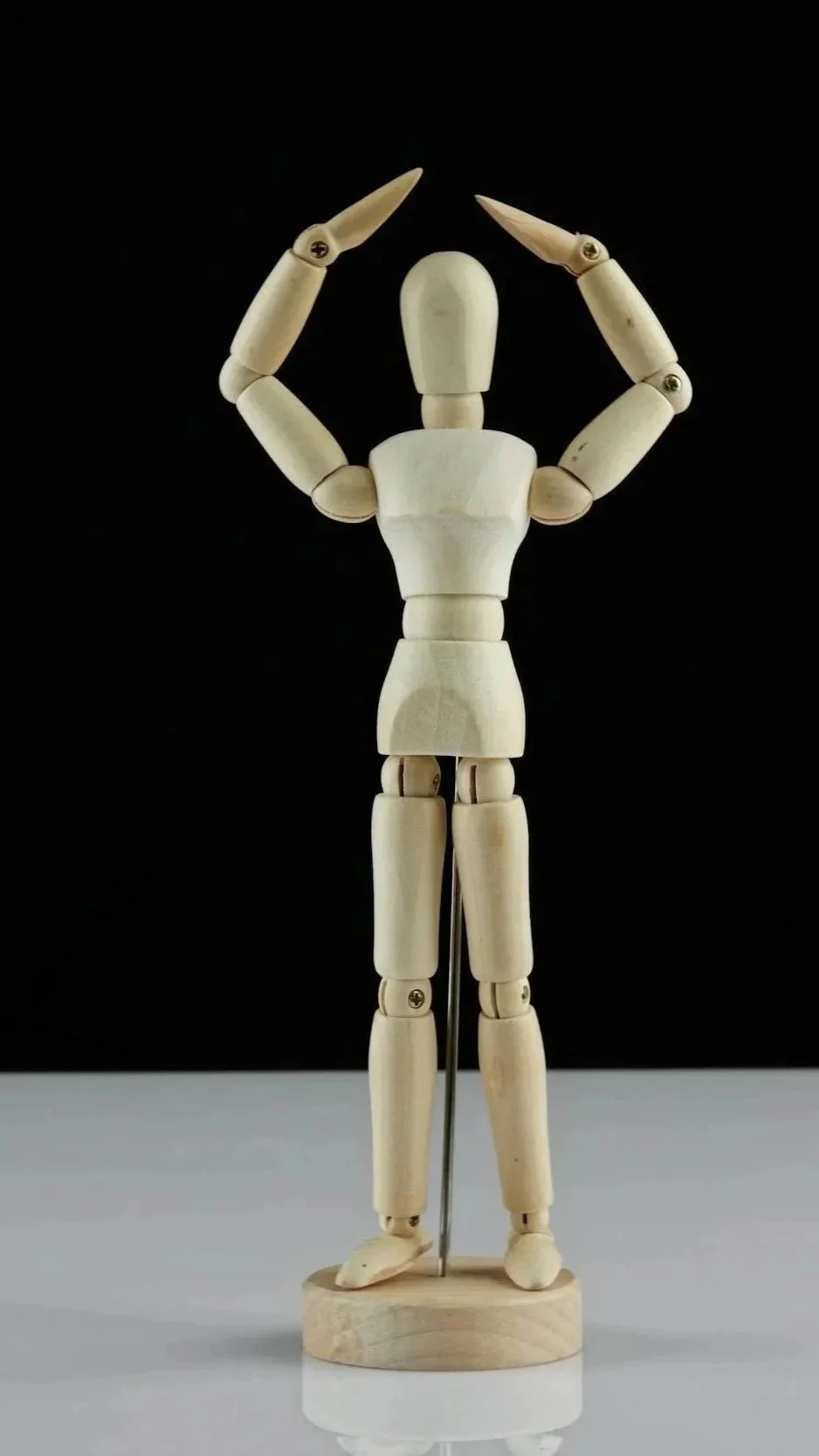 A wooden mannequin posed with arms raised above its head, forming a circle, on a black background. good posture