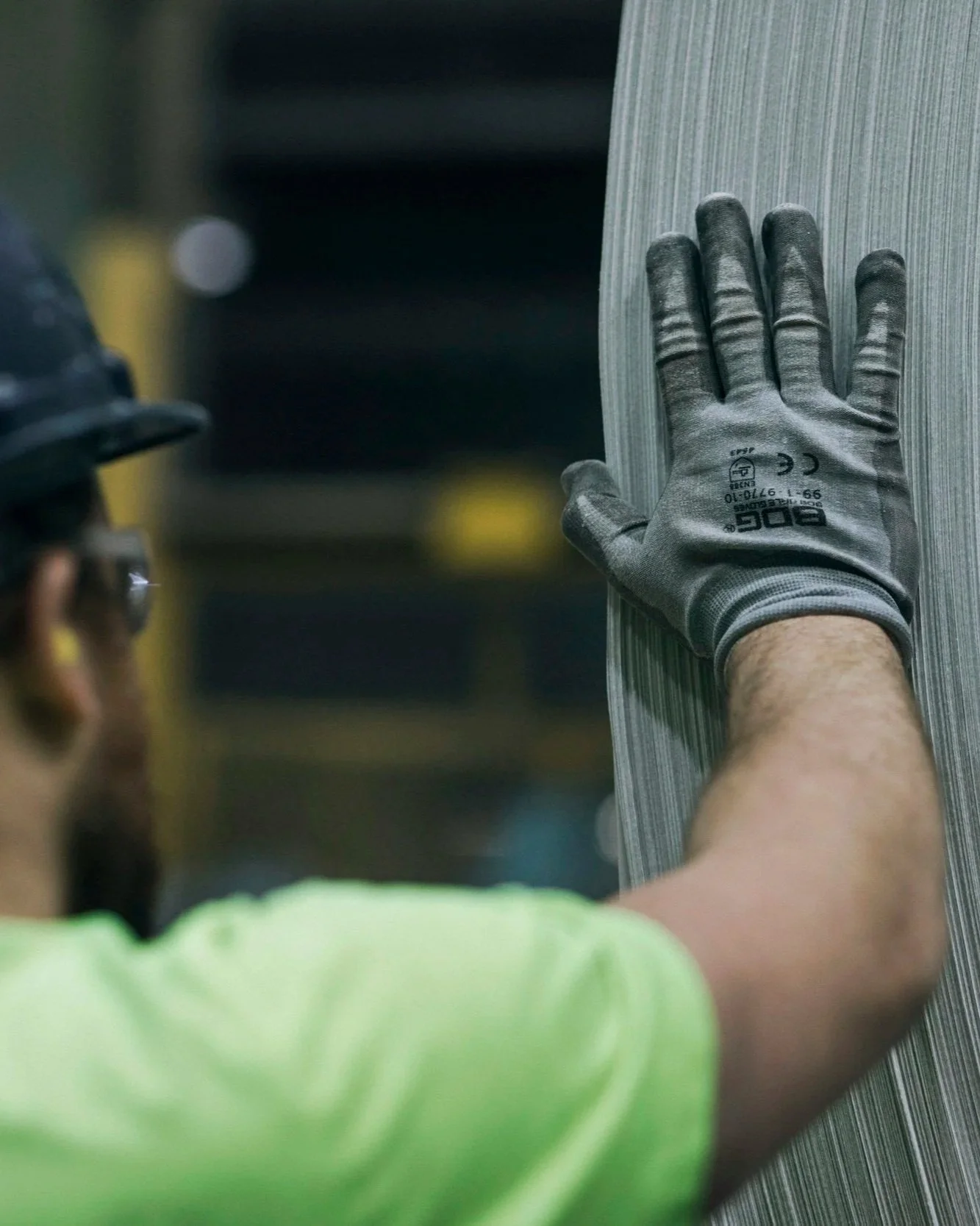 A worker in a high-visibility shirt and gloves is holding a vertical metal panel, possibly at a construction site. Another person is taking a photo of or observing the worker. WSIC workers compensation