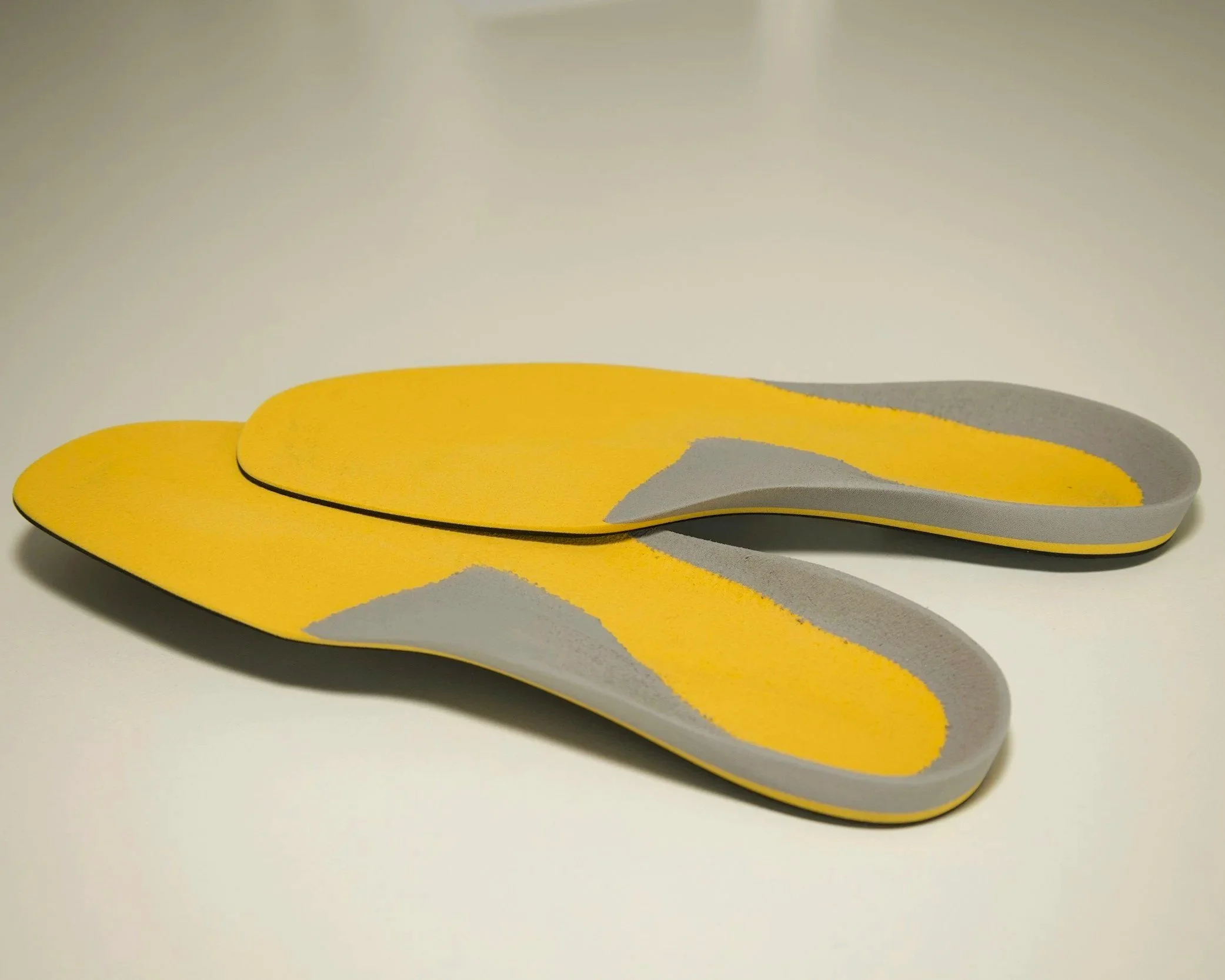 Close-up of yellow and gray foam or felt sheets stacked with a curved pattern. orthotics