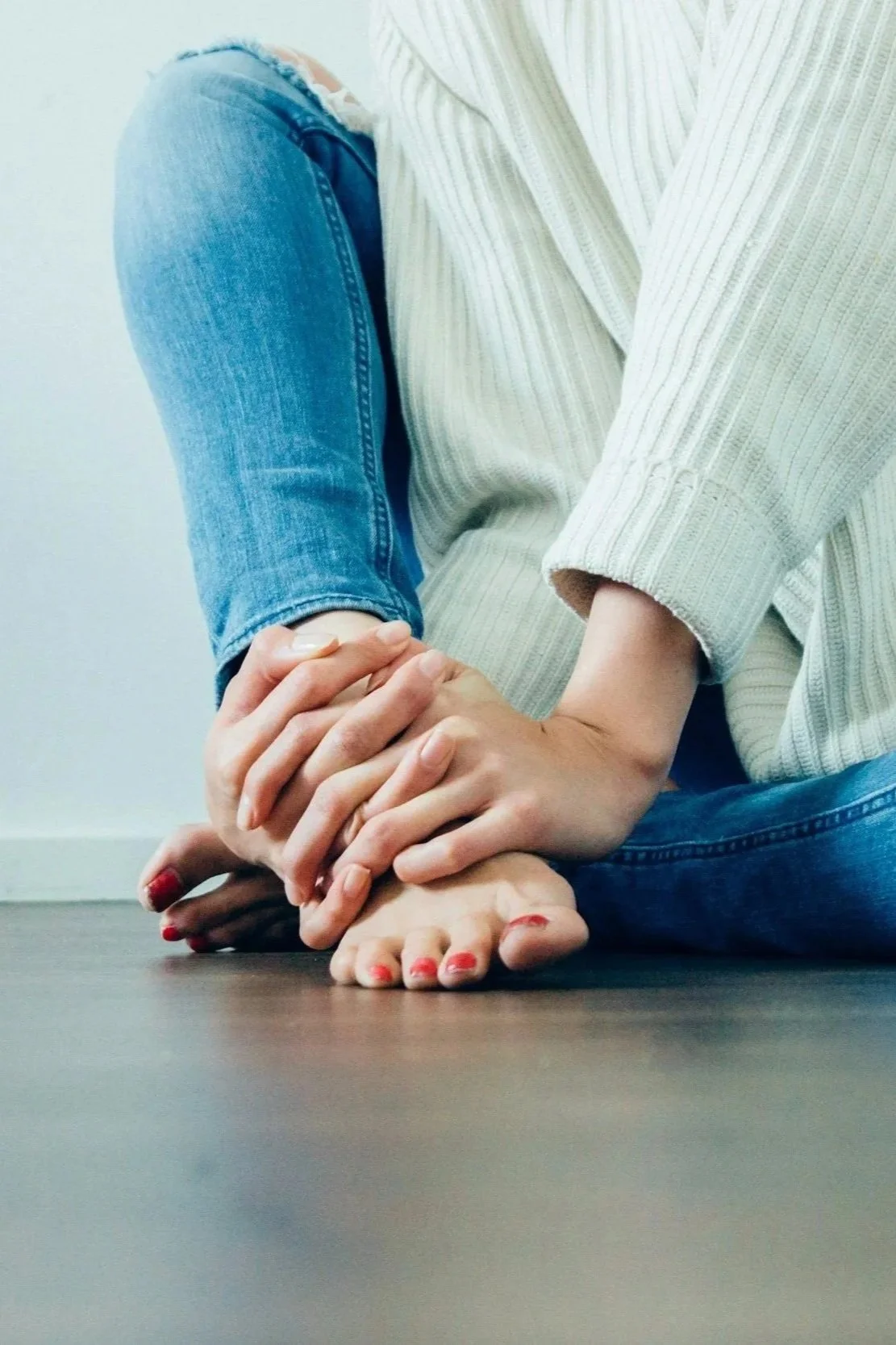 Two people sitting on the floor, holding hands, wearing casual clothes, with one hand resting on the other's foot. foot pain