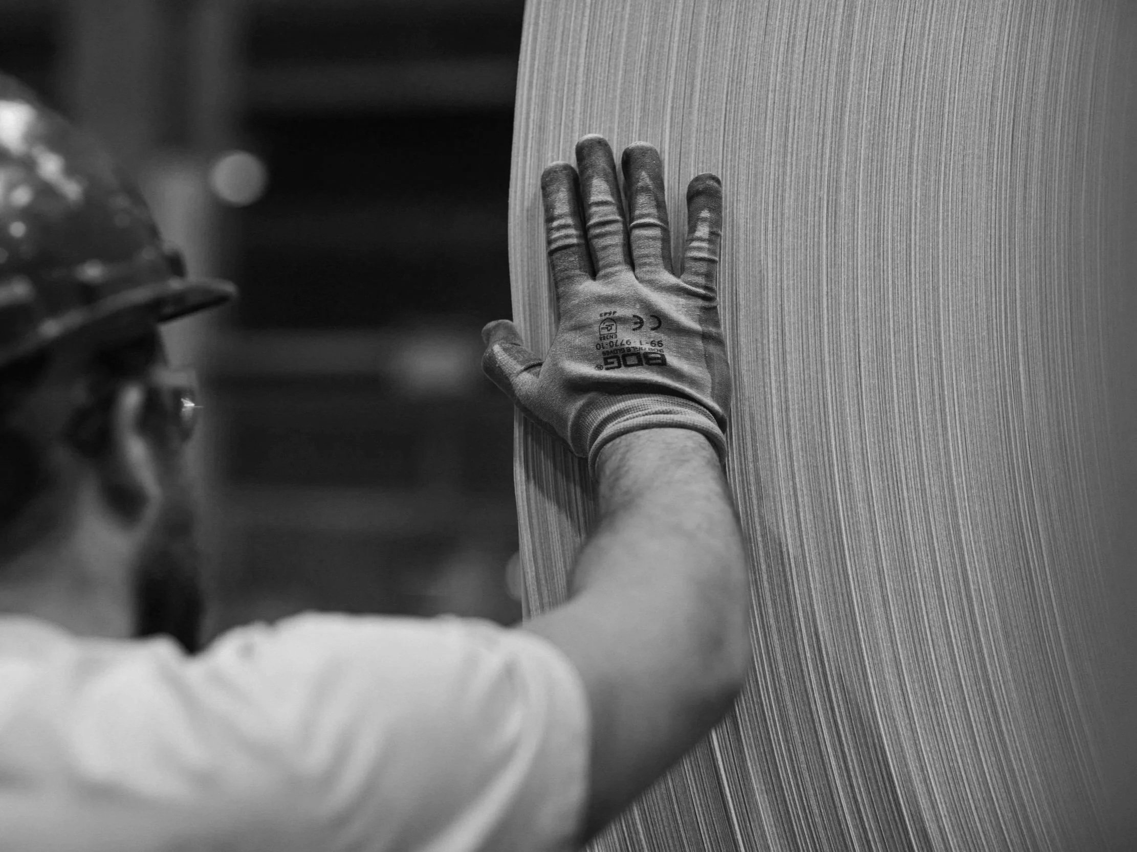 A person's hand wearing a work glove touches a vertical surface with a textured pattern, in black and white. WSIB cases treated