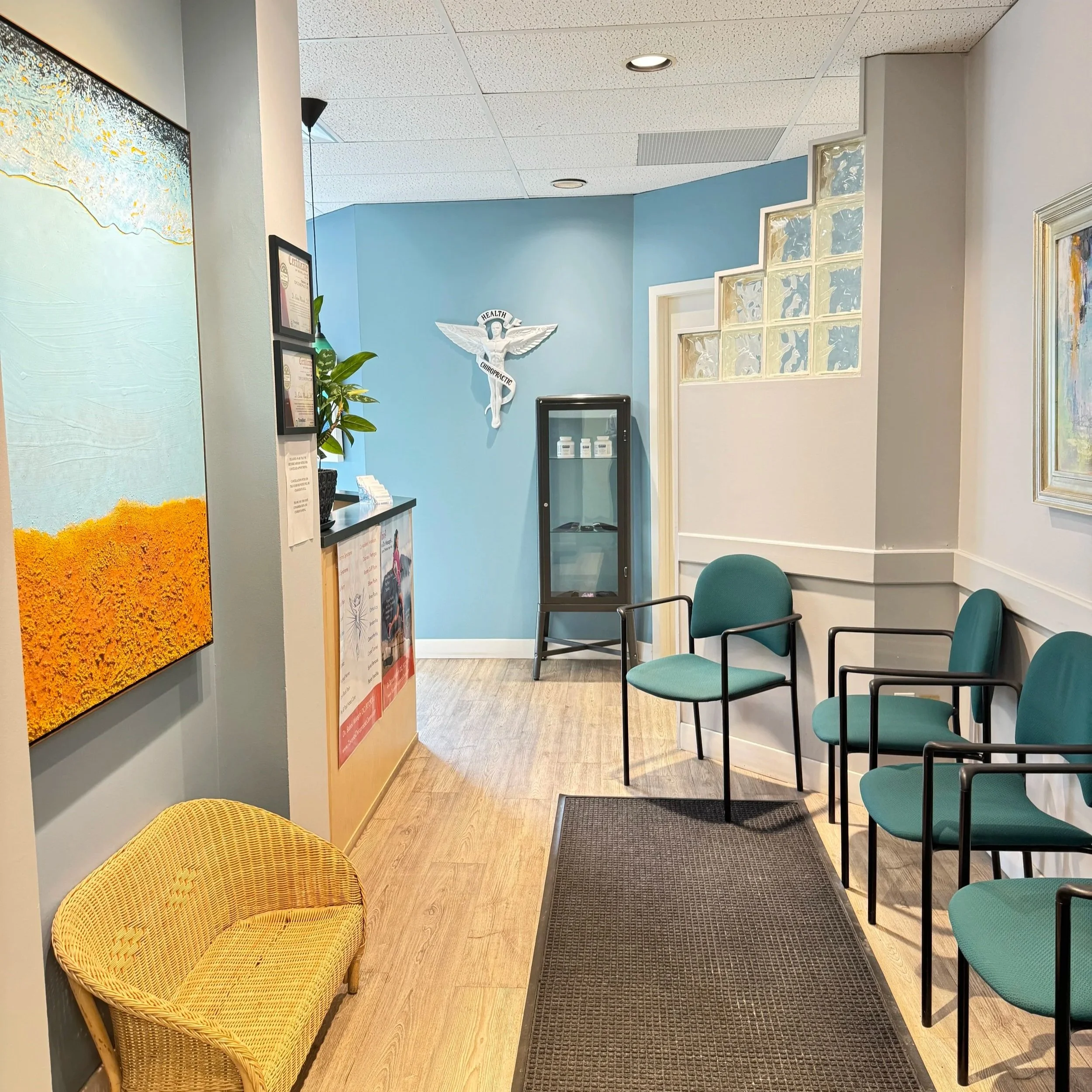 Waiting room with teal chairs, a yellow woven chair, and a blue wall with a white medical symbol and glass block window. reception room dr. missaghi's office