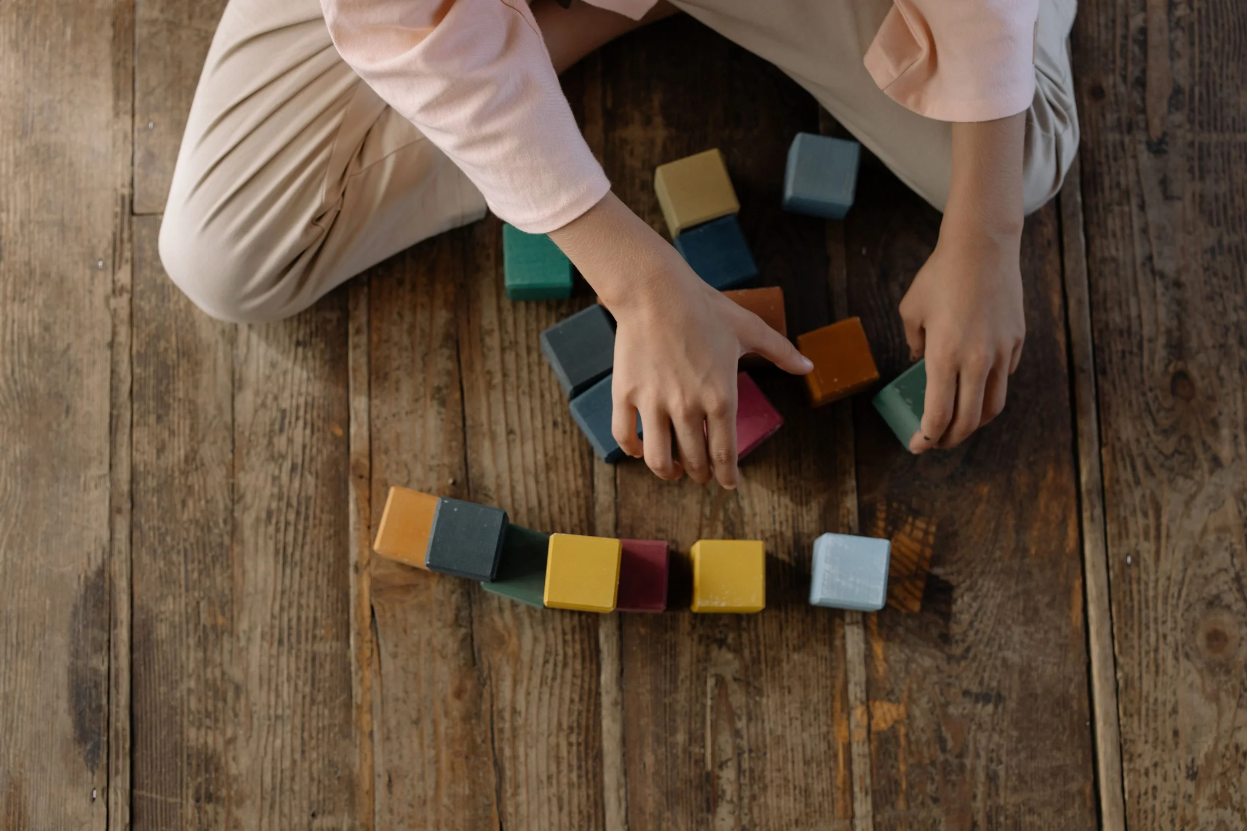 Enfant assis au sol jouant avec des blocs de bois colorés creare une tour ou une structure.