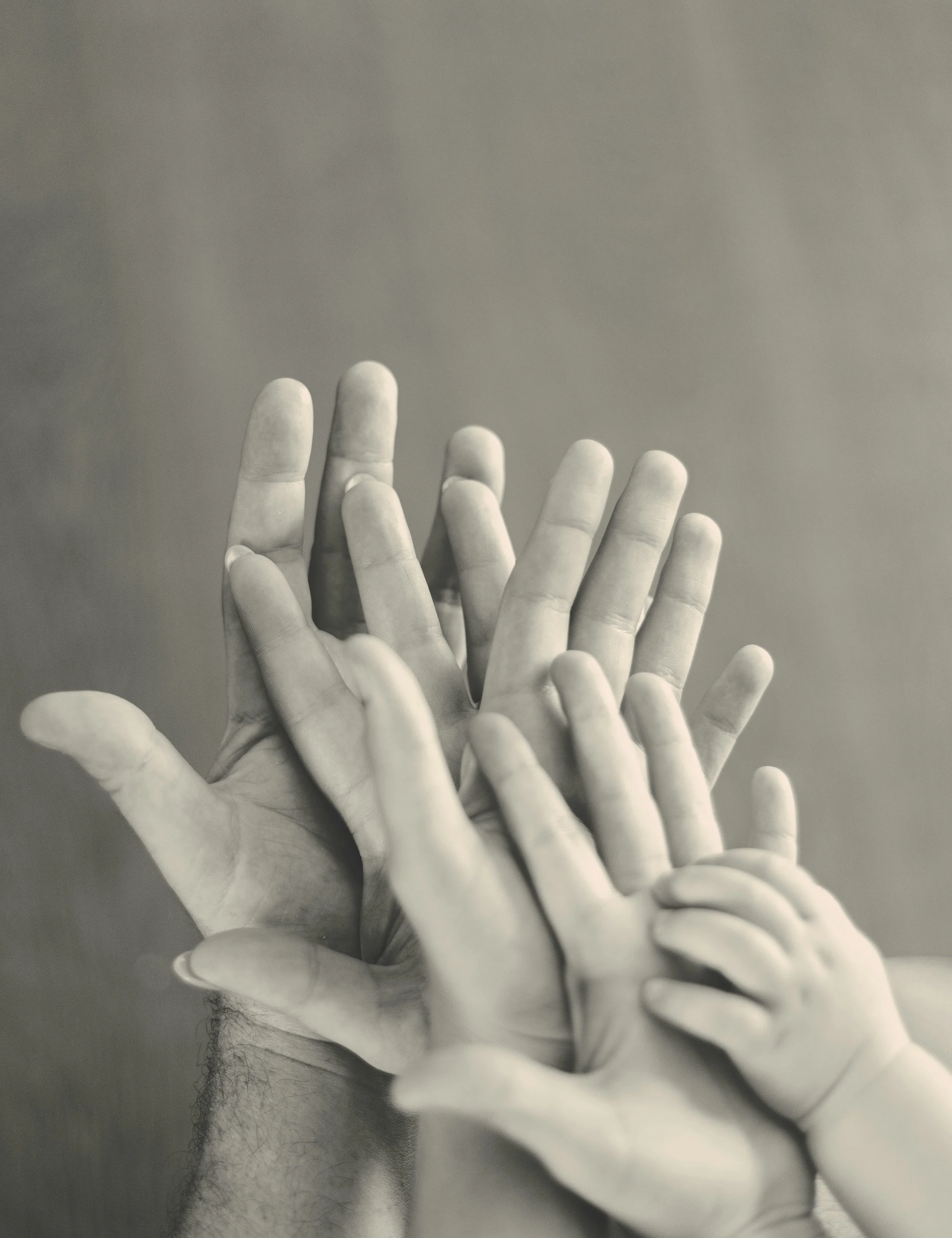 Deux mains en latex blanc qui se touchent, une autre main se déployant au centre, toutes les mains sont posées sur une surface plane, avec un fond gris neutre.