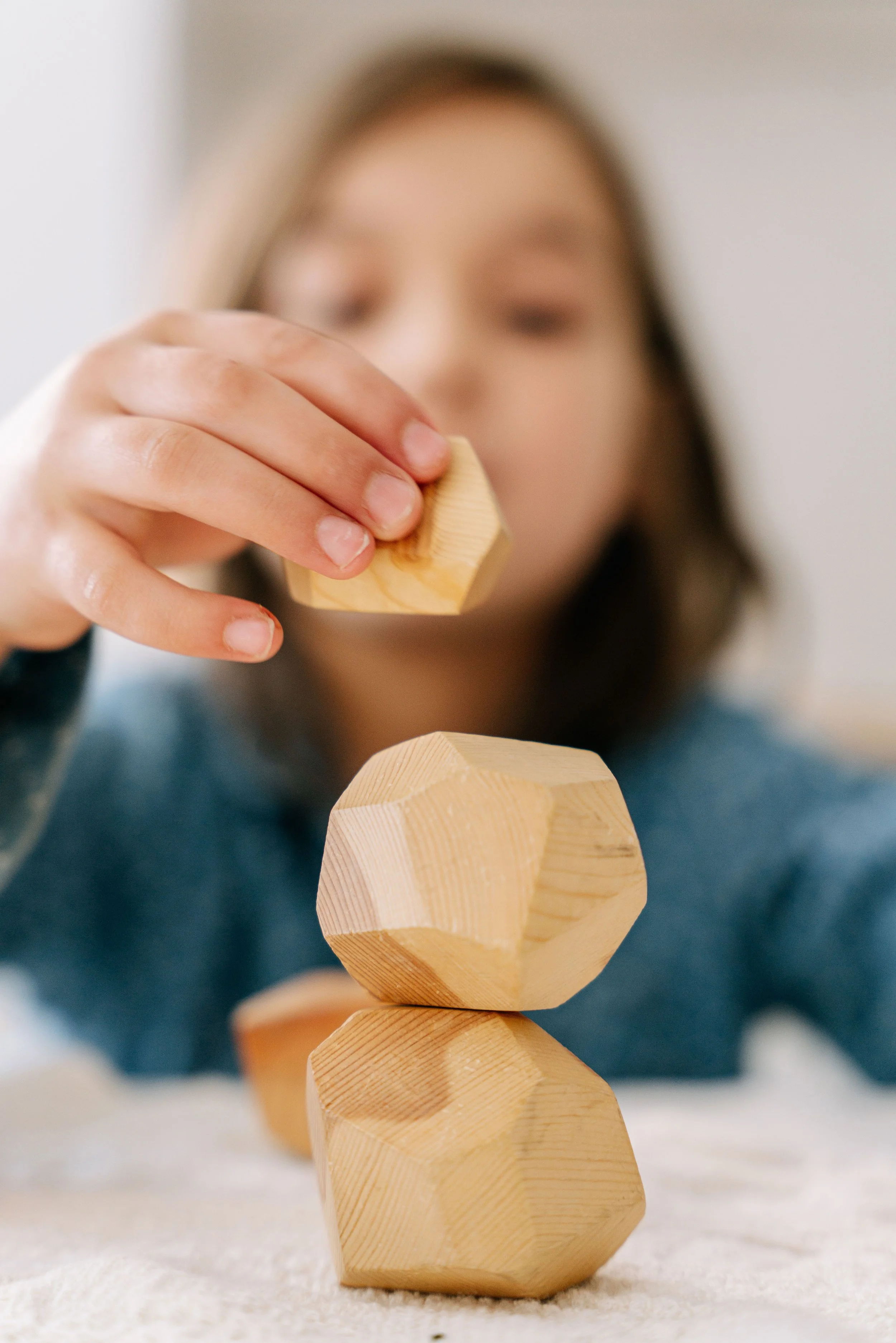 Une personne place une pièce de bois en forme d'hexagone sur une structure en bois composé de plusieurs autres formes géométriques en bois, avec un fond flou.