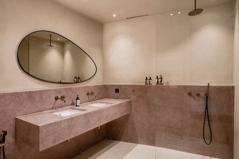 Modern bathroom with a double sink vanity, oval mirror, and a rainfall showerhead.