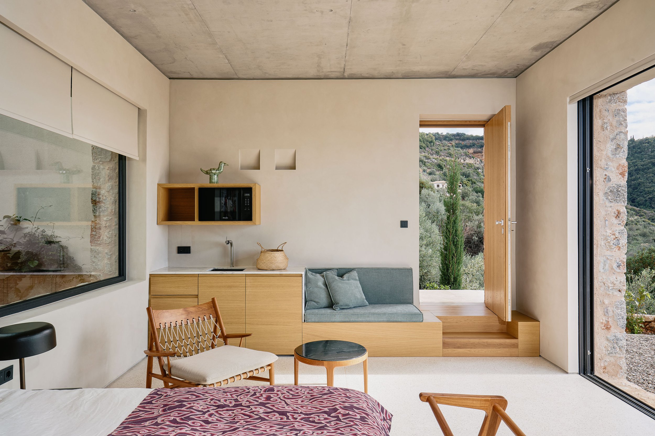 Modern living room with large glass doors opening to a scenic hillside view, beige walls, minimalist decor, and a cozy seating area.