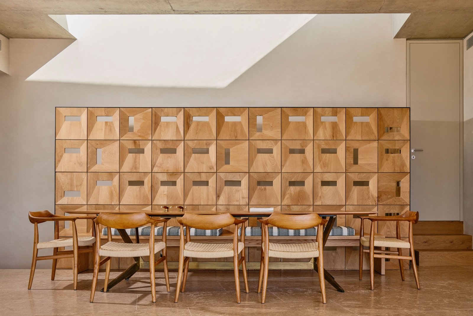 A wooden wall with a geometric pattern, a dining table, and six wooden chairs in a modern dining room.