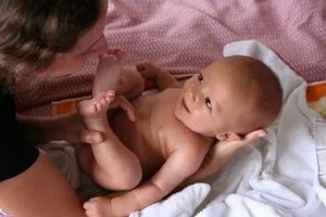 Bébé allongé sur un lit, regardant une femme qui le tient par la main.