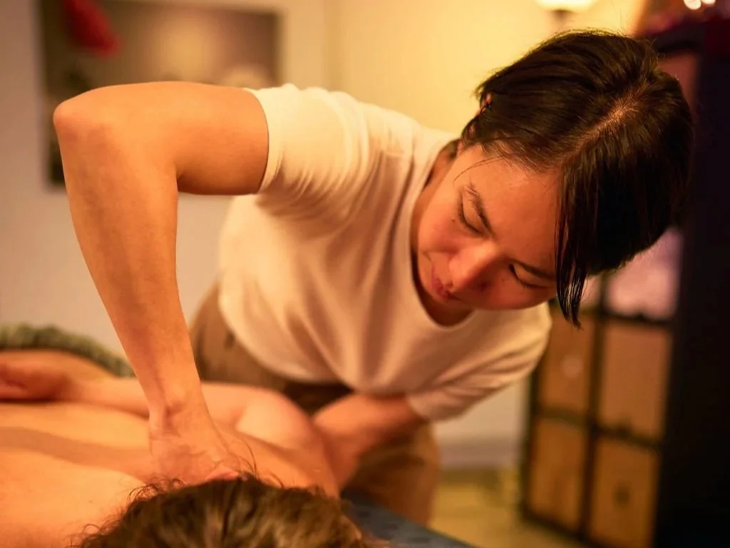 Une femme donne un massage à une autre personne sur un lit dans une pièce chaleureuse.
