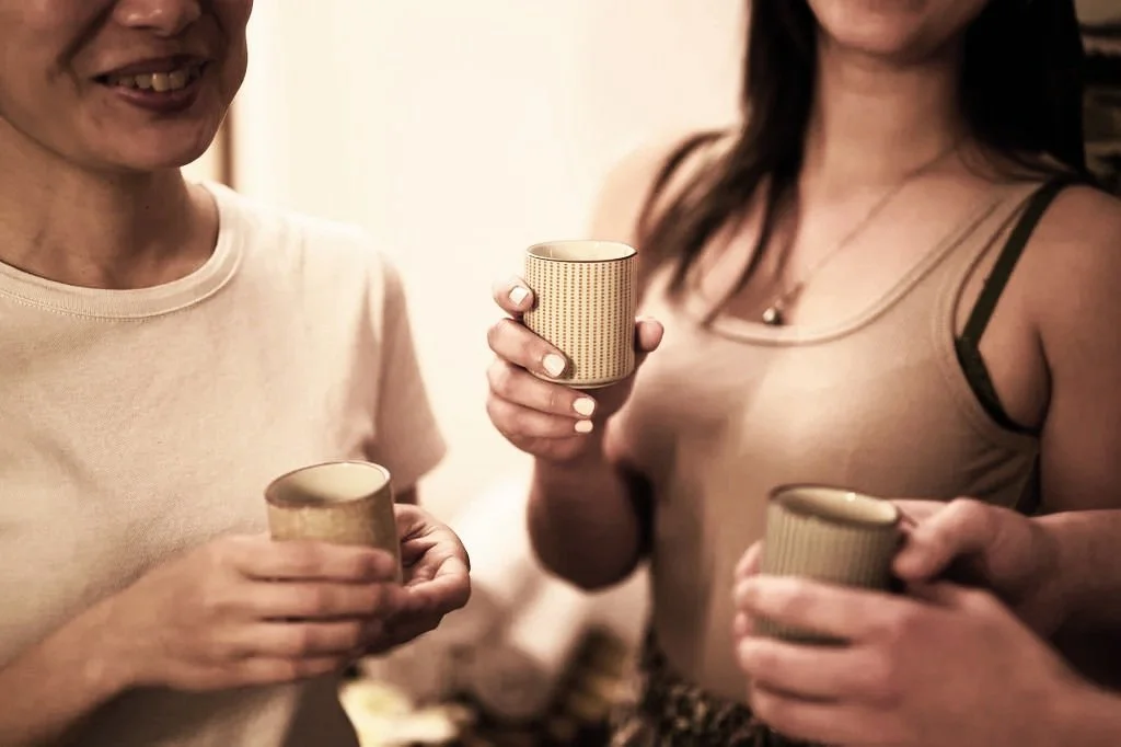 Deux femmes souriantes tenant des tasses en céramique lors d'une réunion ou d'une conversation.