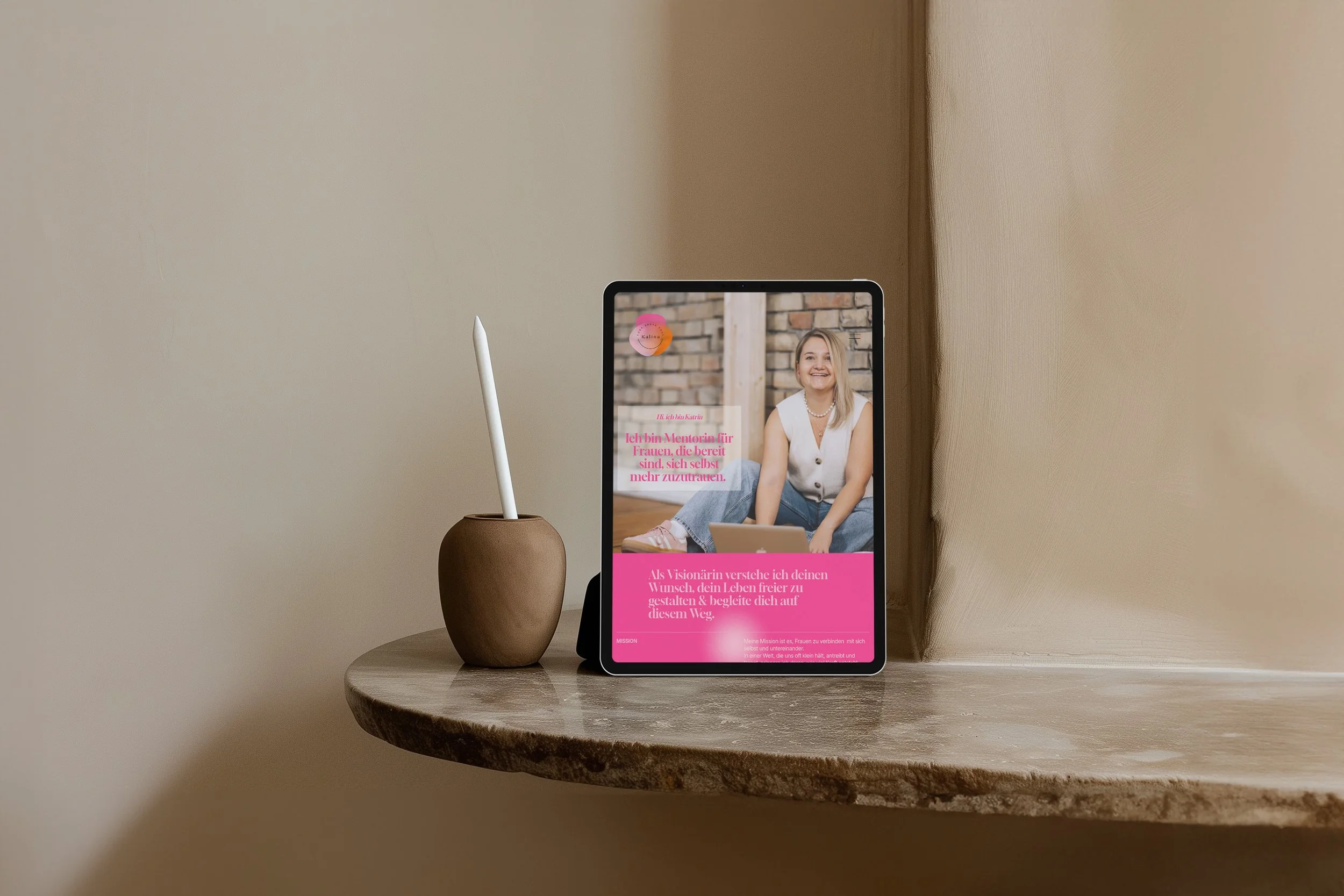 Tablet mit einem Bild einer lachenden Frau, die auf dem Boden sitzt, auf einem Holzbrett, mit einem Text in Pink darüber, neben einer Vase mit einem Stift, auf einem runden Holztisch.