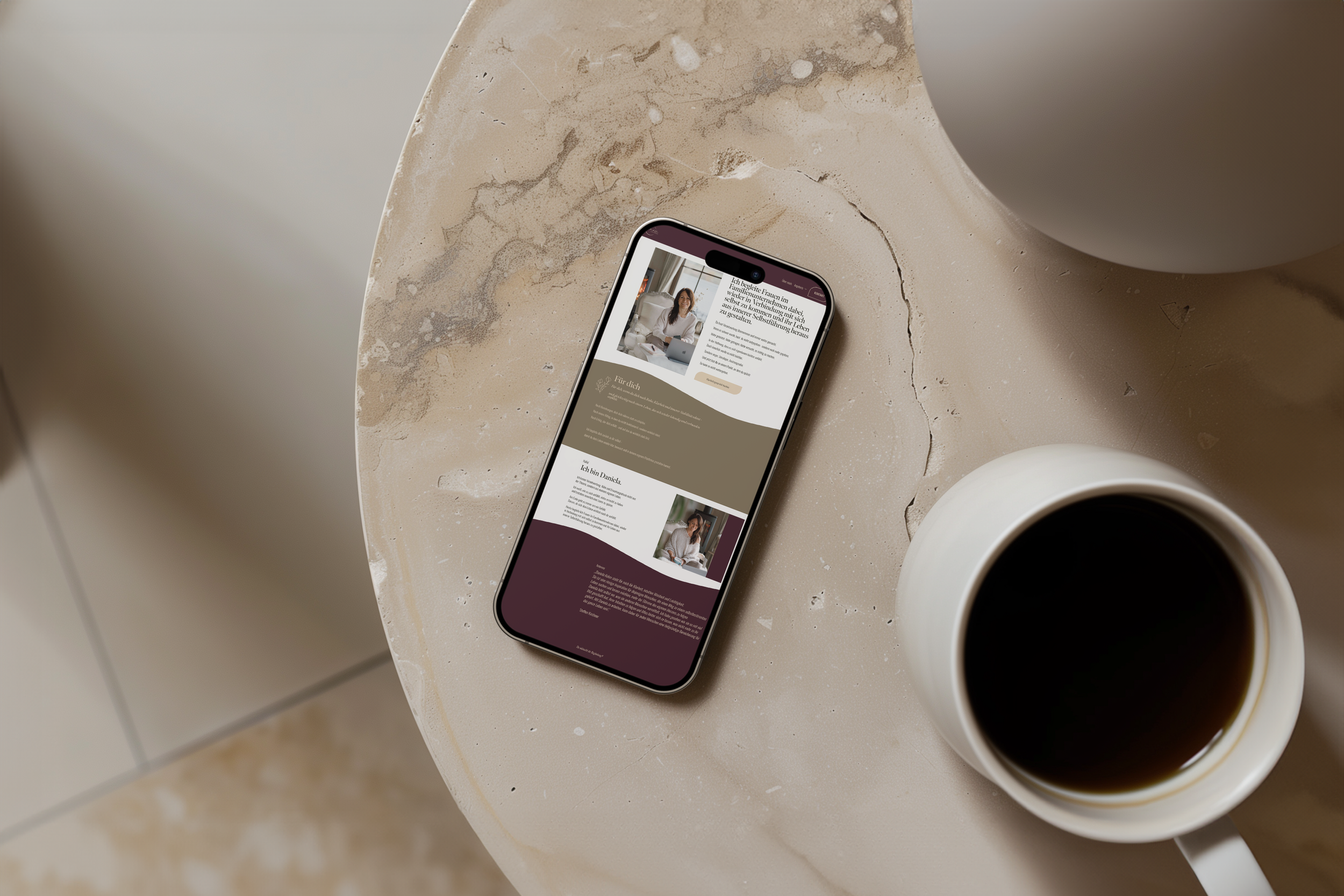 Smartphone liegt auf einer beige Marmor-Tischplatte, zeigt eine Webseite, neben einer weißen Tasse mit schwarzem Kaffee.