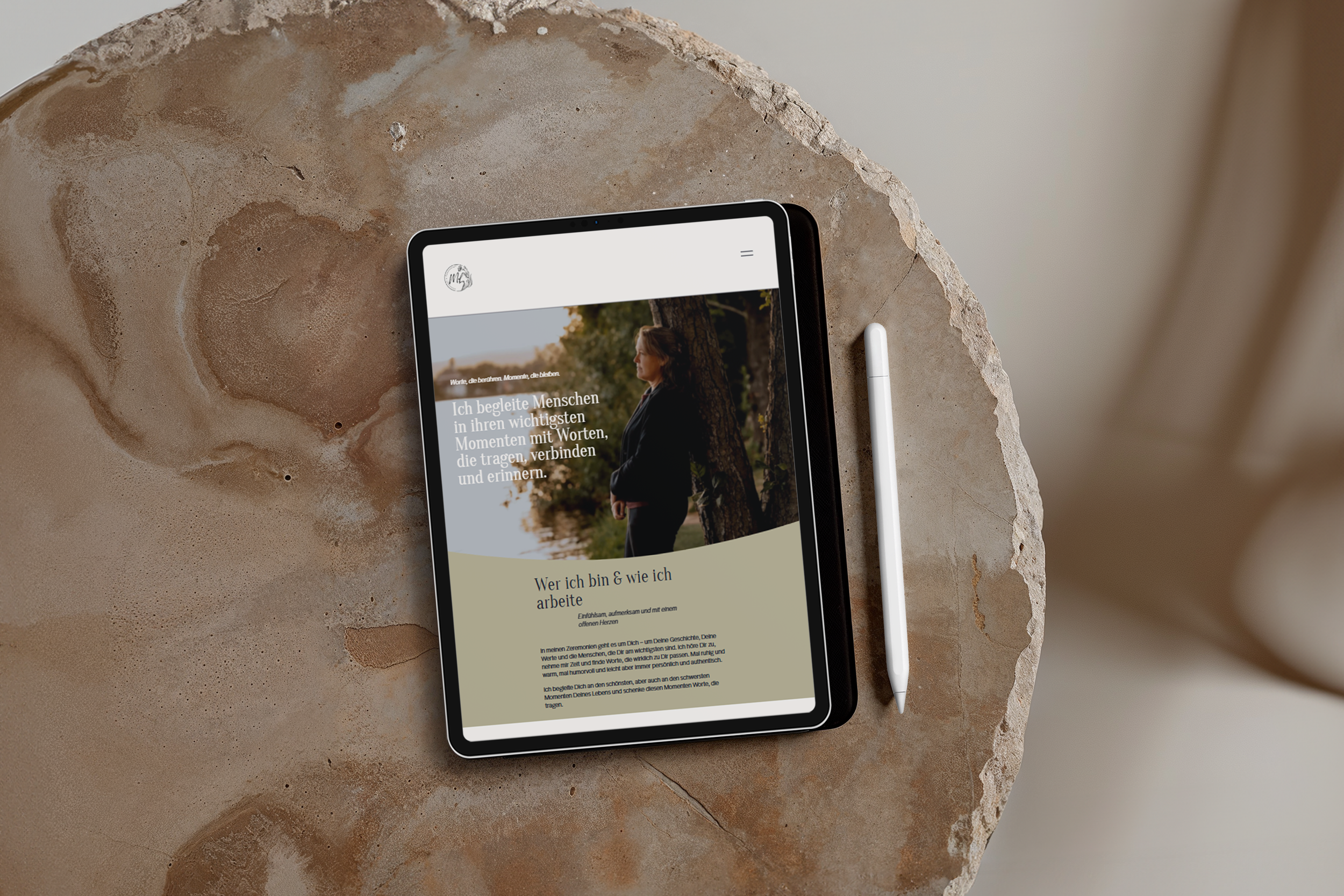 Ein Tablet mit einem Website-Design, das eine Frau im Freien zeigt, neben einem weißen Stylus auf einem Marmor-Tisch.