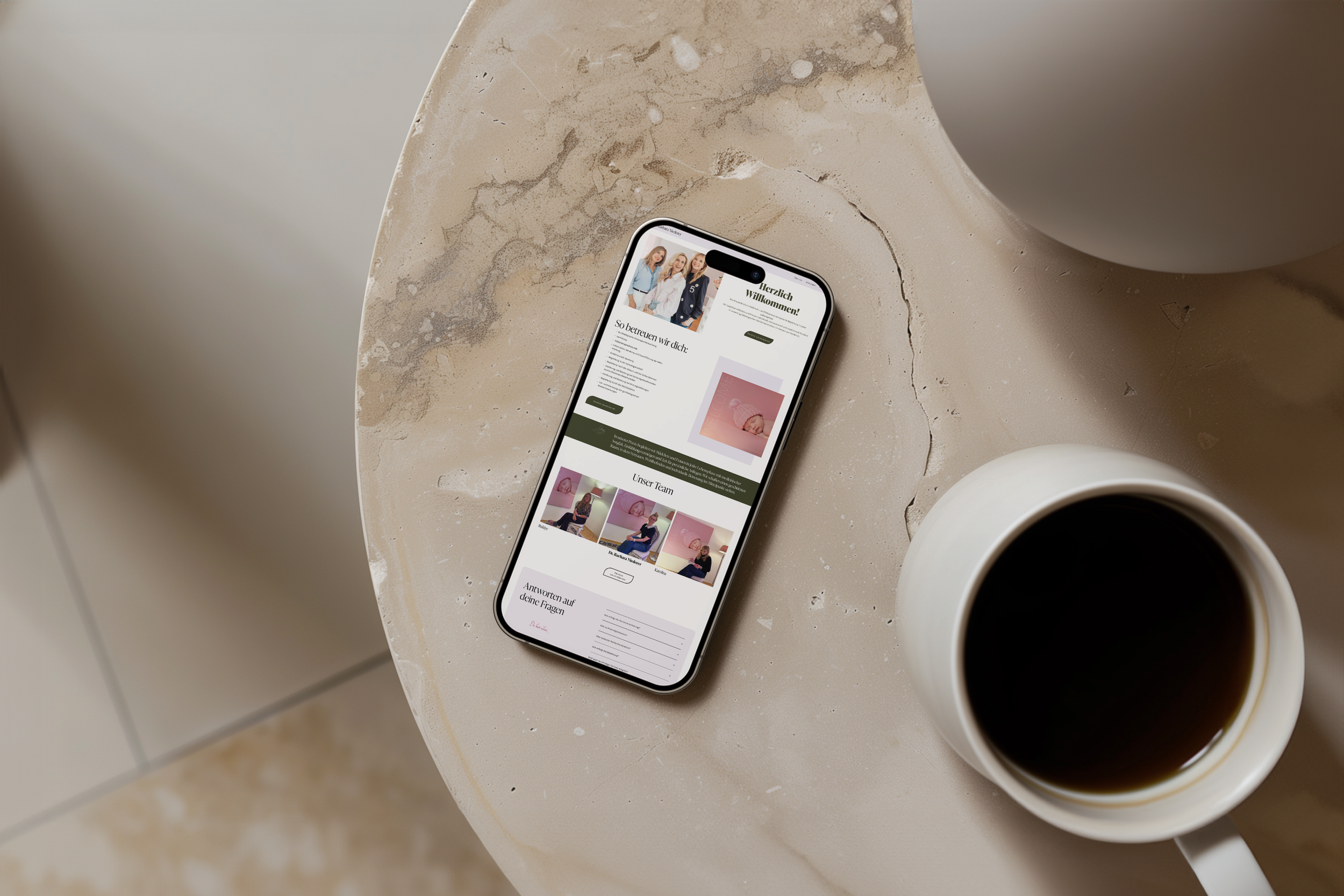 Ein Smartphone liegt auf einer Marmor-Tisch, daneben eine Tasse Kaffee. Das Smartphone zeigt eine Webseite mit einem Bild von drei Frauen und Text auf Deutsch.