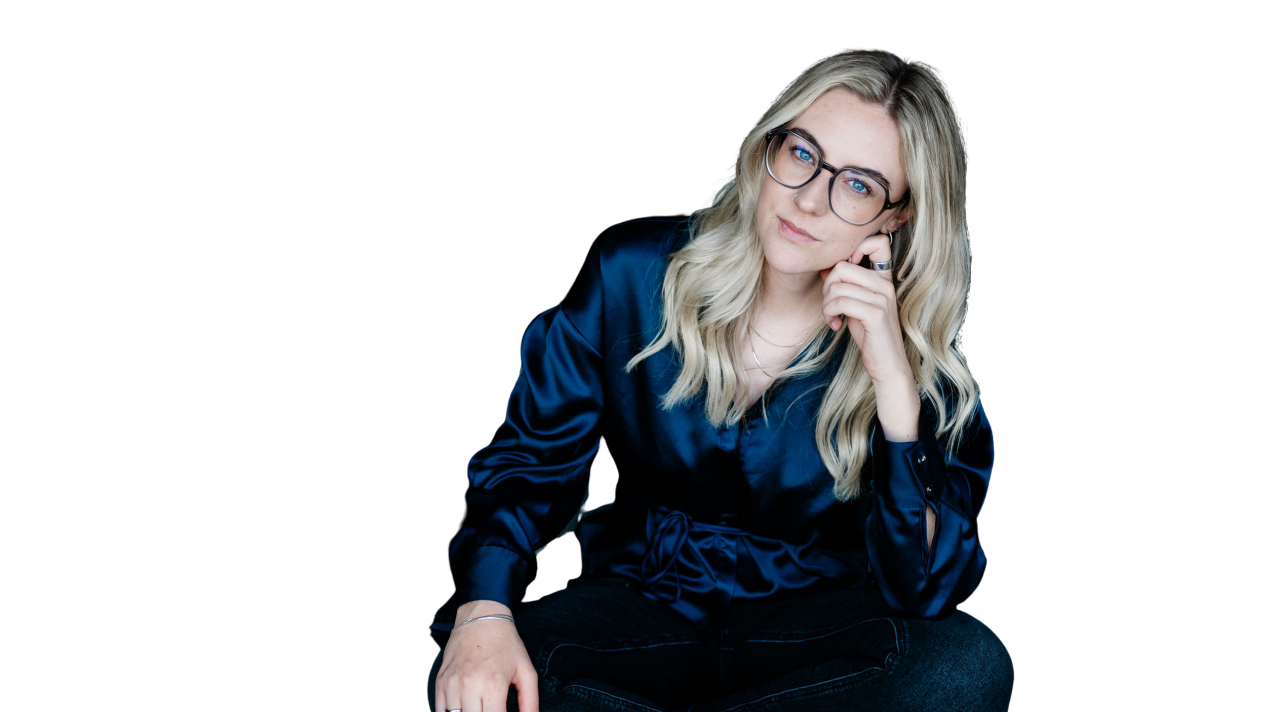 Eine junge Frau mit blonden, lockigen Haaren, trägt Brille, ein silbernes Nasenpiercing und einen blauen Satin-Blazer, sitzt vor schwarzem Hintergrund.