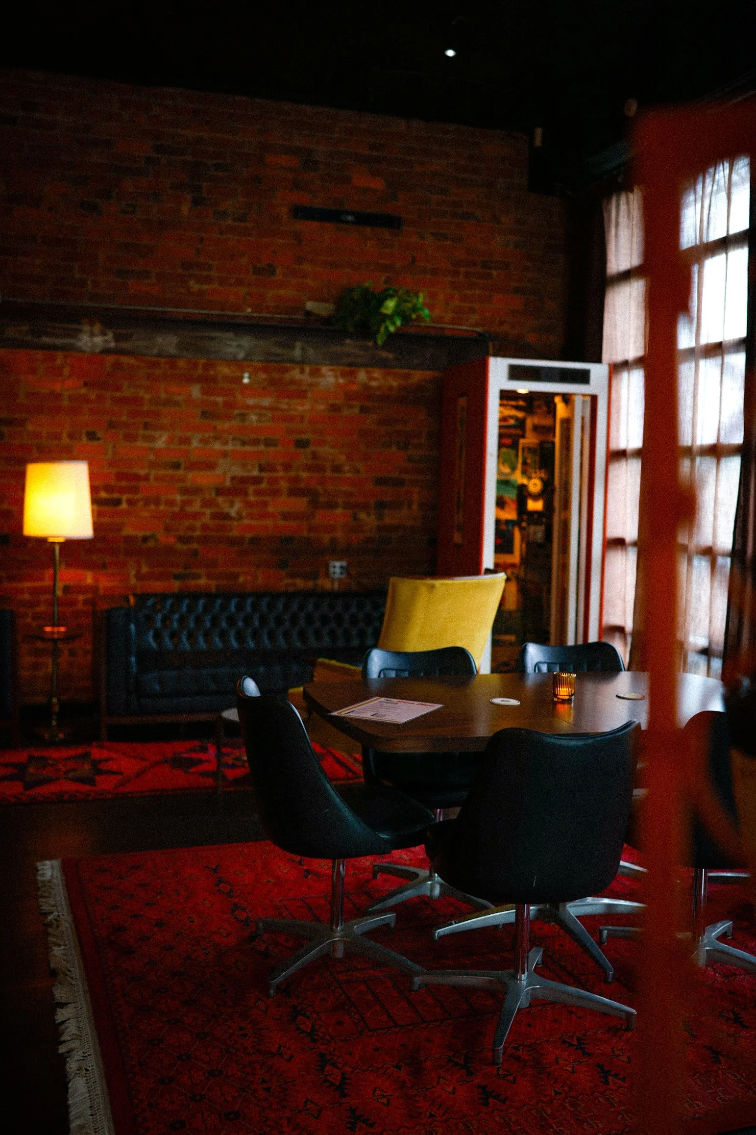 Leather sofa, phone booth, and table by large windows in a cozy lounge area of the bar