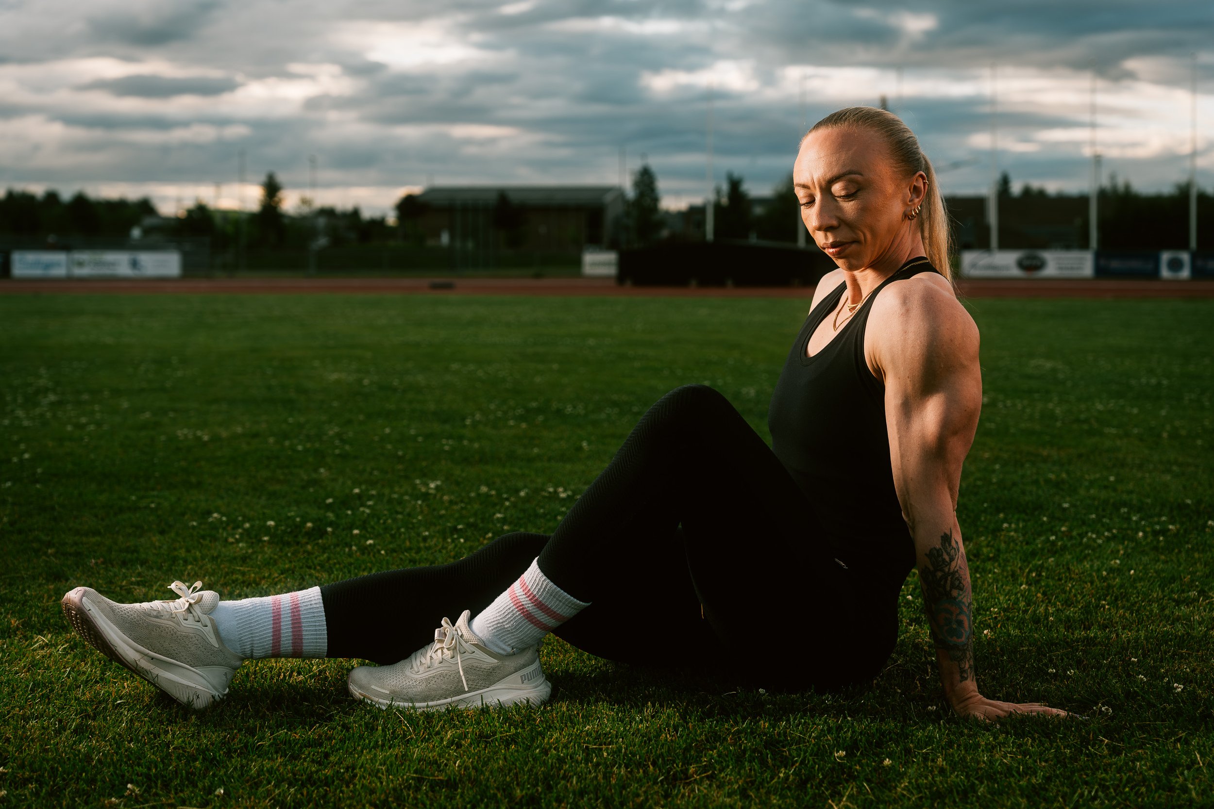 Sportportrett av en kvinne på friidrettsbane ved solnedgang med atletisk uttrykk.