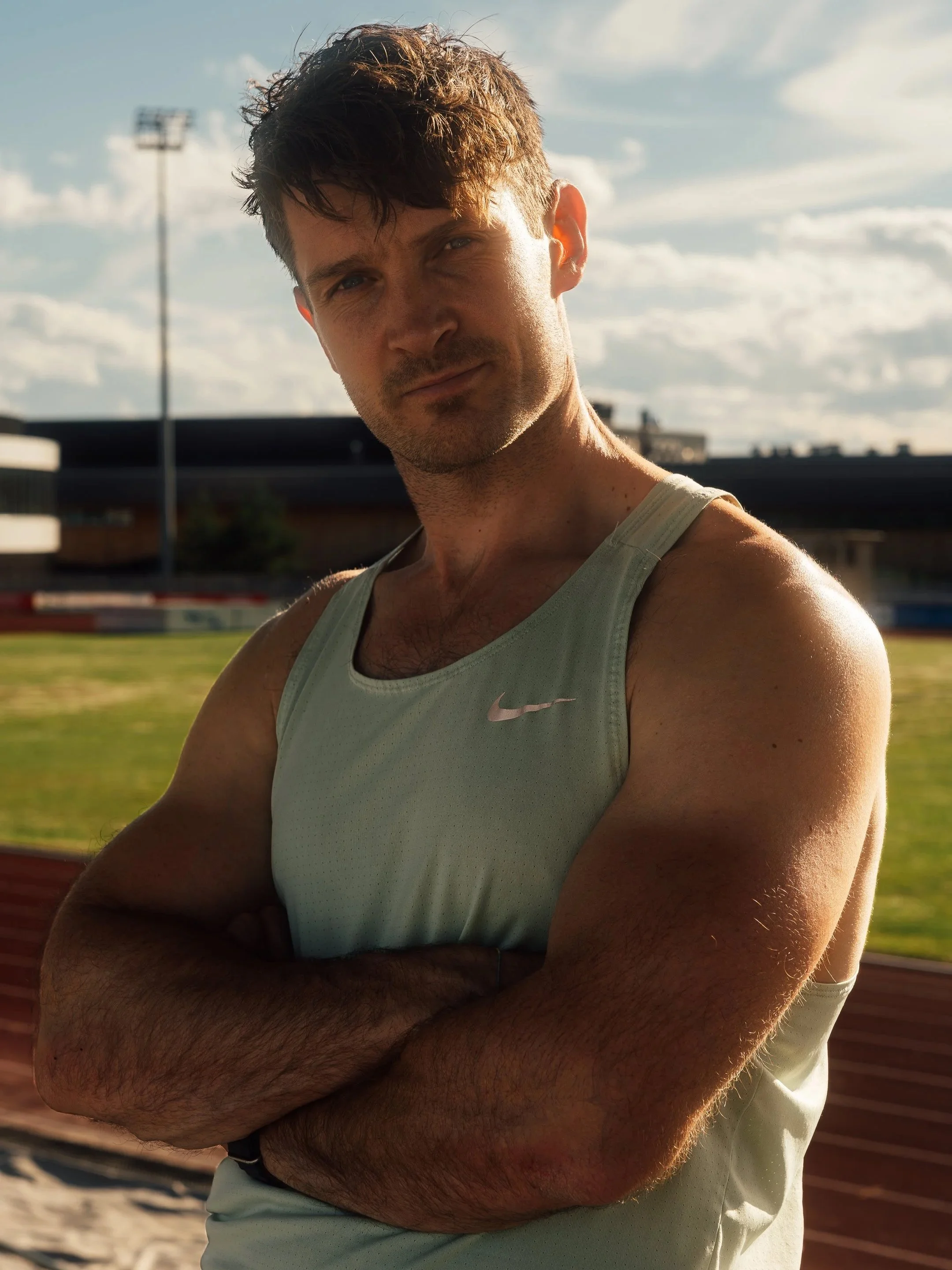 Sportsportrett av en muskuløs mann i singlet med armene i kors på en friidrettsbane.