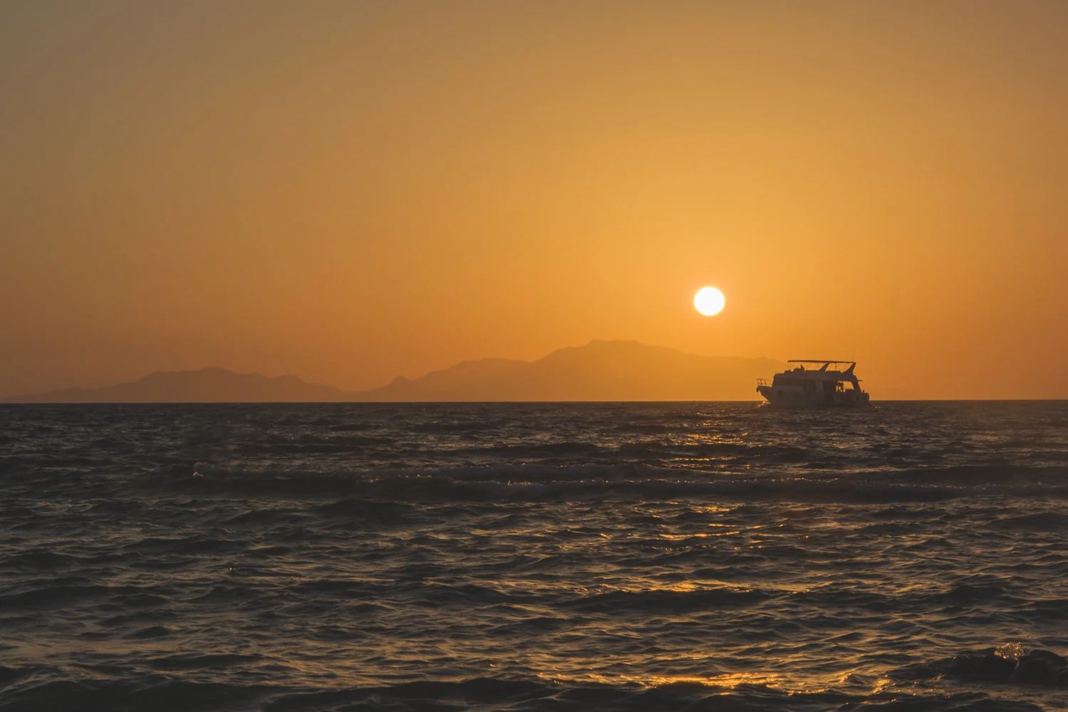 Solnedgang over havet med båt i silhuett ved horisonten
