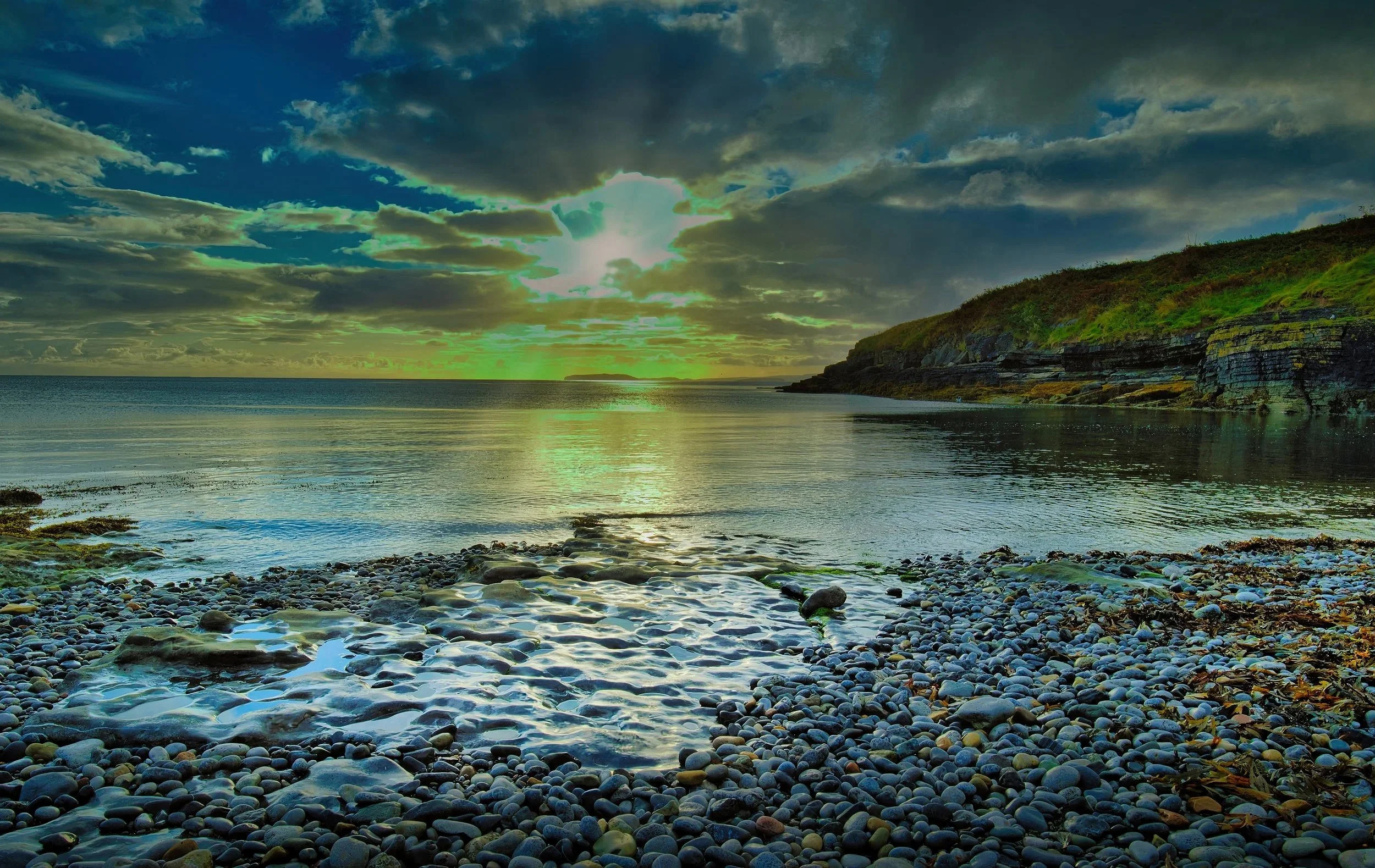 Sunrising over a glassy pebble beach, Golden Sundays light up the clouds and the glistening seashore