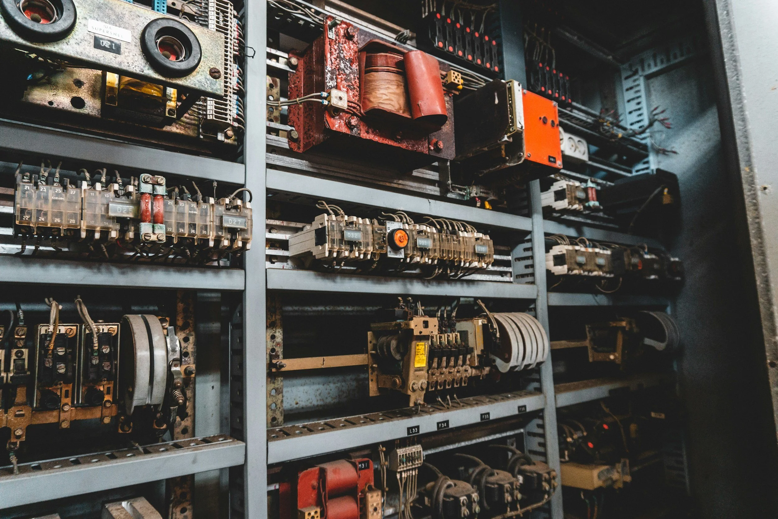 An industrial electrical control panel with various wiring, relays, transformers, and circuit components mounted on metal shelves.