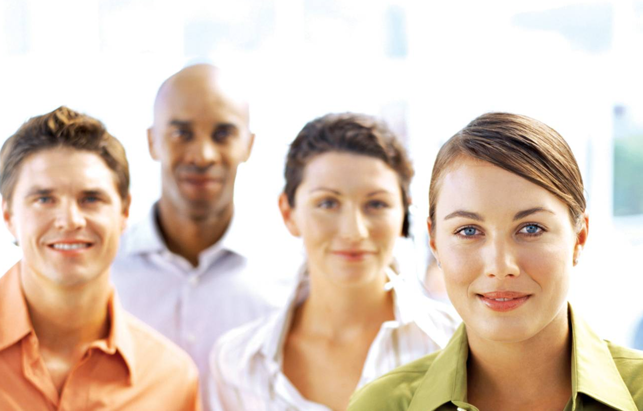 Group of four diverse young adults standing indoors, smiling at the camera.