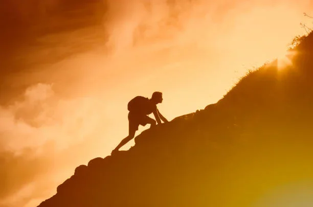 Silhouette of a person climbing a hill or mountain at sunset or sunrise.