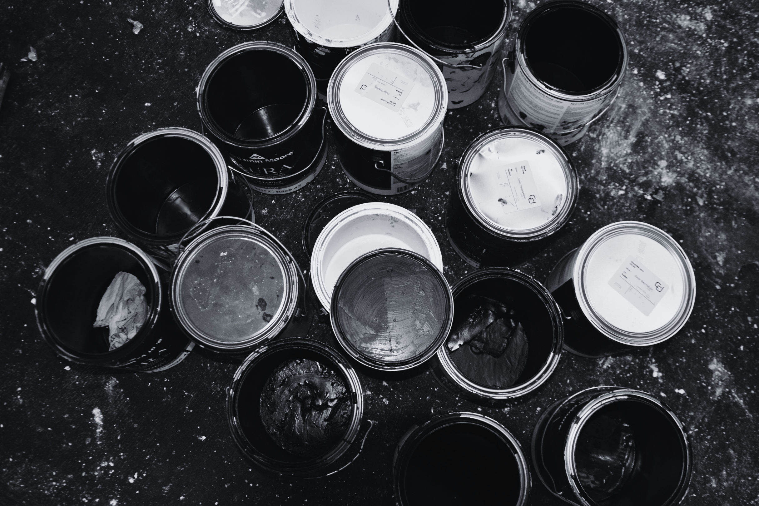 Black and white photo of open cans of paint scattered on a dirty surface