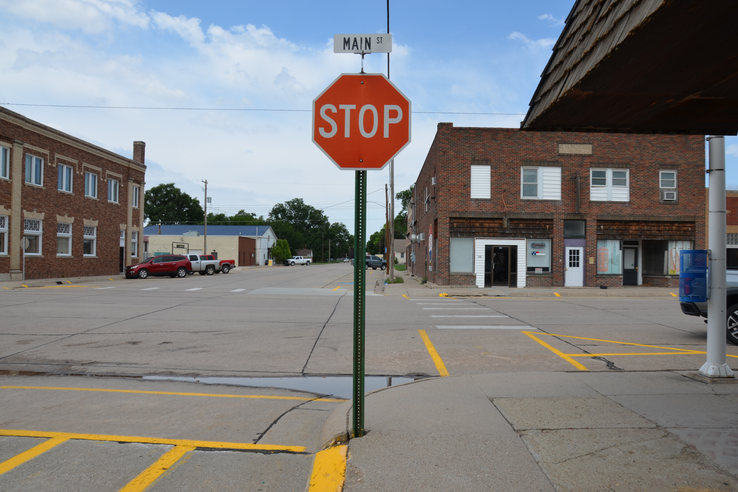 Street intersection with a stop sign, a Main Street sign, and surrounding buildings, parked cars, and a clear sky.