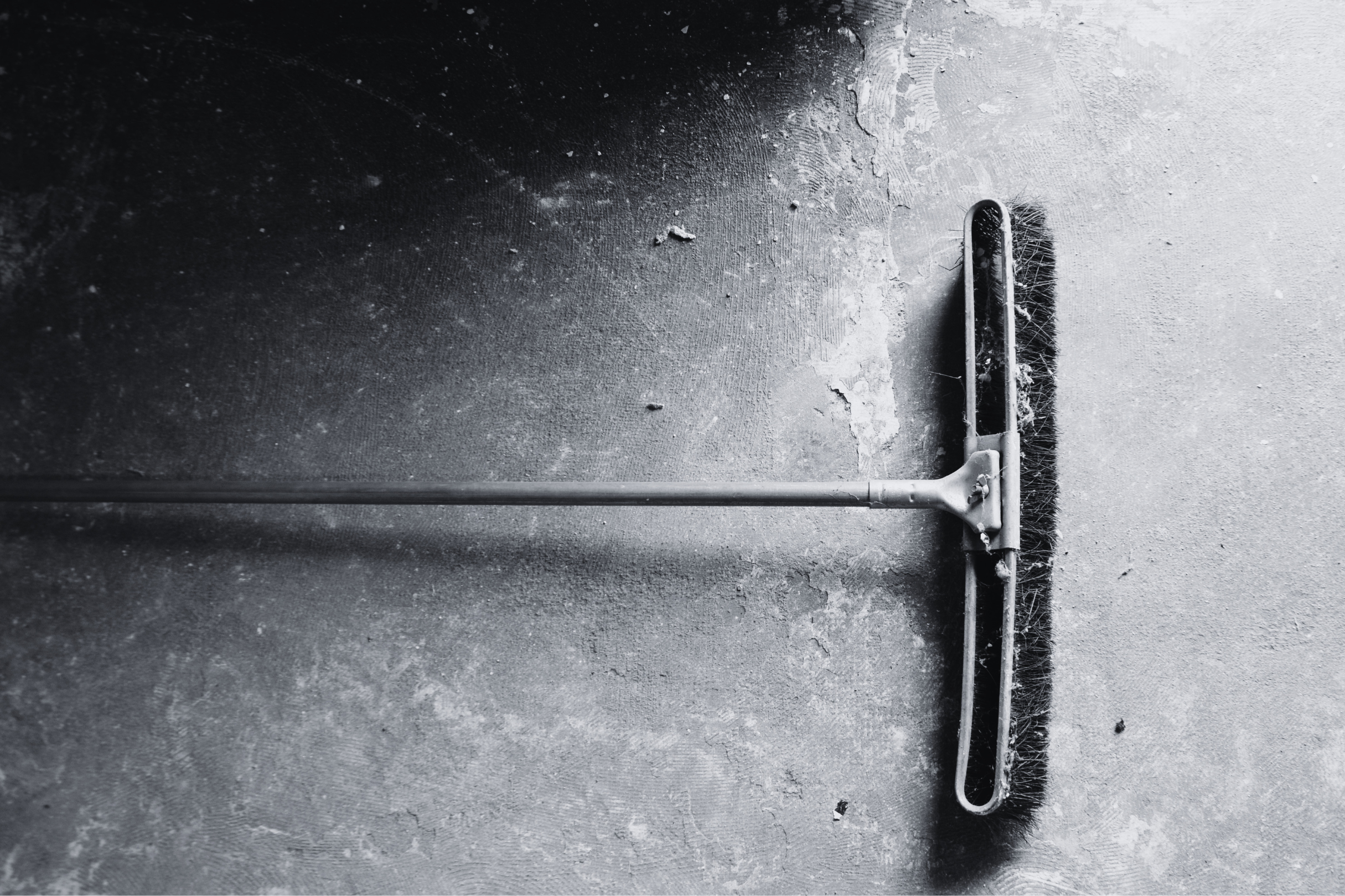 Black and white photo of a floor squeegee cleaning a textured surface, with dirt and debris visible around and underneath it.