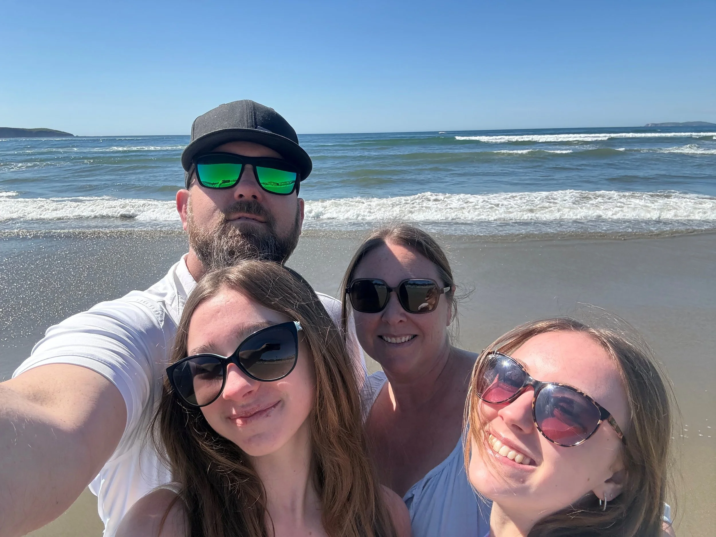 Group of people taking a selfie at the beach on a sunny day with waves in the background.