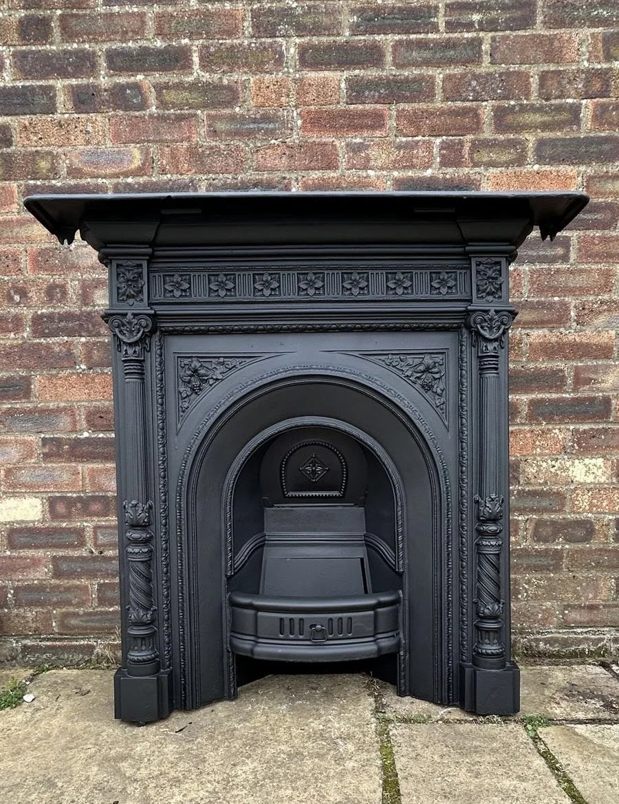 A vintage black cast-iron fireplace with ornate decorative details. Victorian-inspired design. Lovingly restored, ready to add vintage charm to your home.