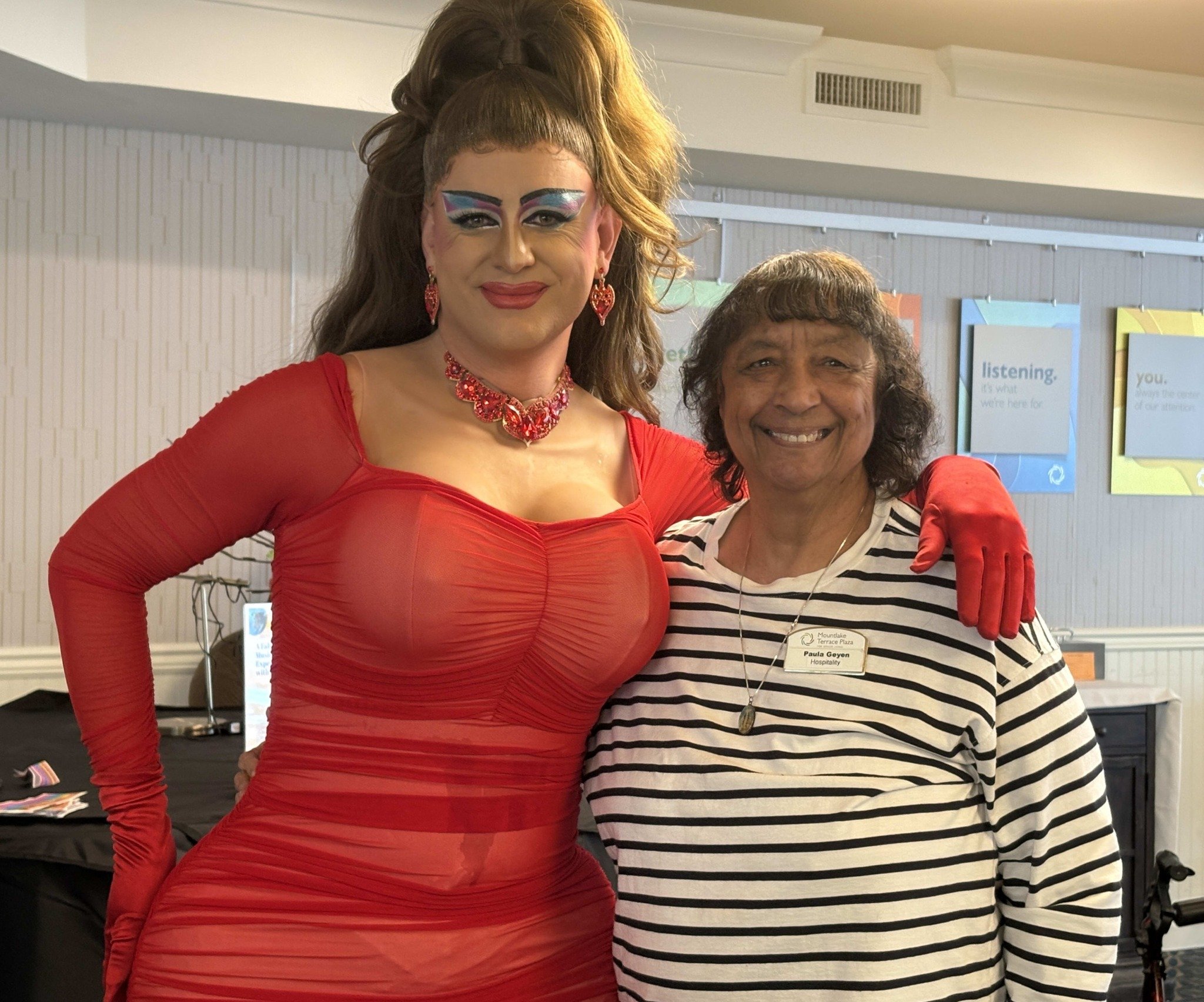 A senior standing together with a drag queen with colorful makeup dressed in red.