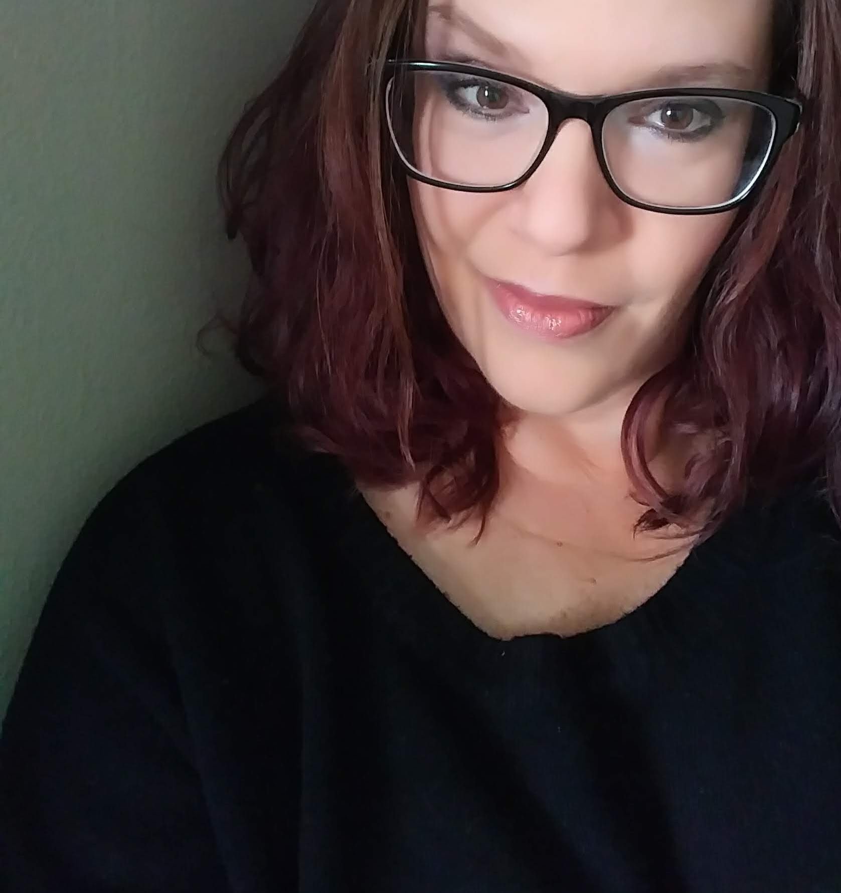 Headshot of Author Carlie Yates with black glasses and a black top with red hair.