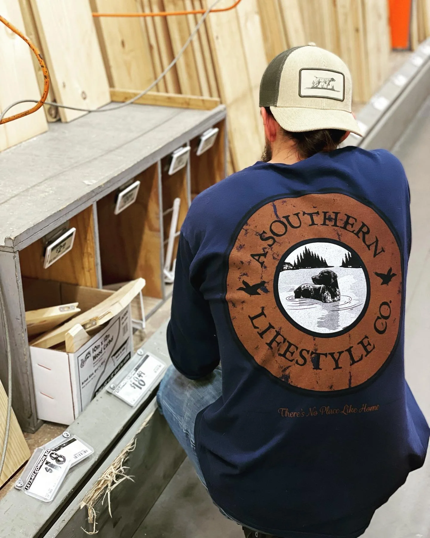 A man wearing a blue jacket with a Southern Lifestyle logo on the back, shopping for wood in a hardware store.