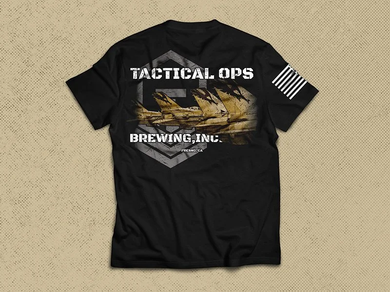 Black T-shirt with a military aircraft graphic and text 'Tactical Ops Brewing Inc.' and 'Fresno, CA' on the back, with a white American flag patch on the sleeve.