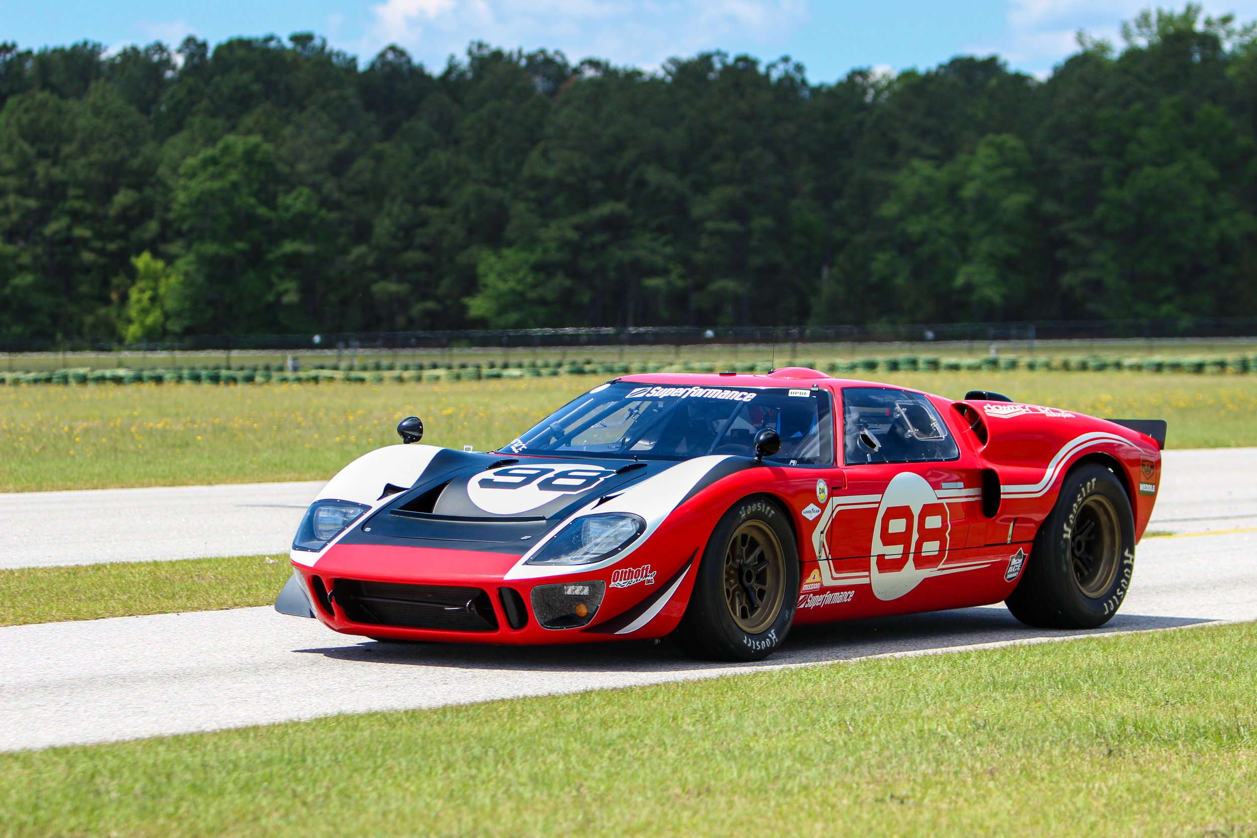 A red and white race car driving on a track with green trees in the background.