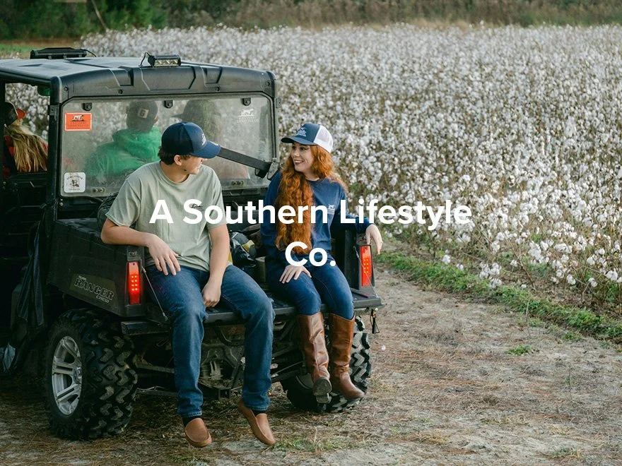 Two young people sitting on the back of a utility vehicle, smiling and talking, in a cotton field during the day.
