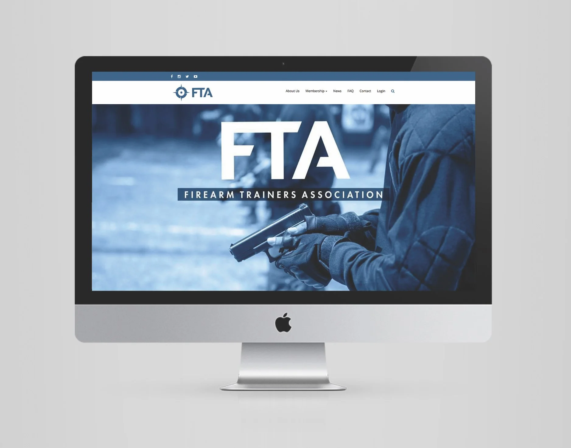 Apple iMac computer displaying the Firearm Trainers Association website with a person holding a handgun.