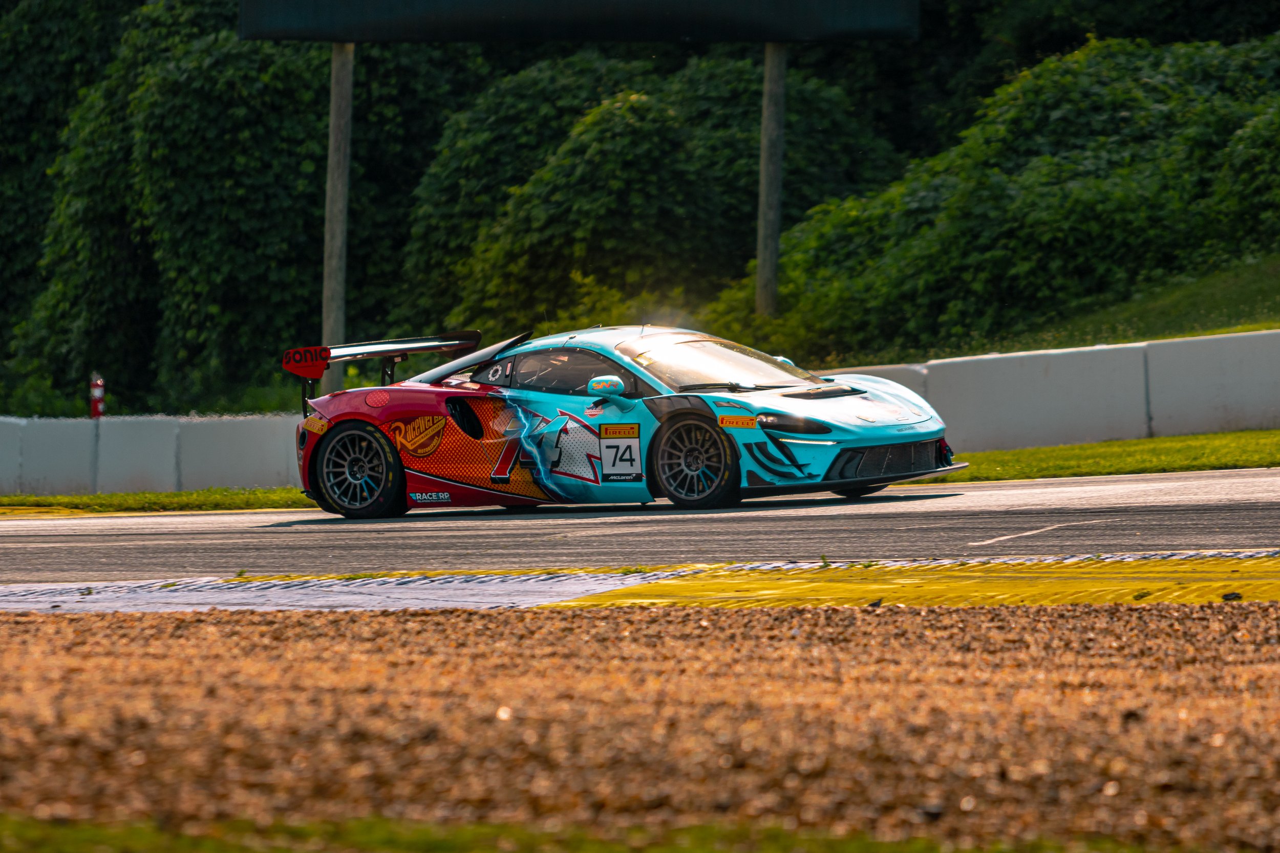 Colorful race car on a racing track with green trees in the background.