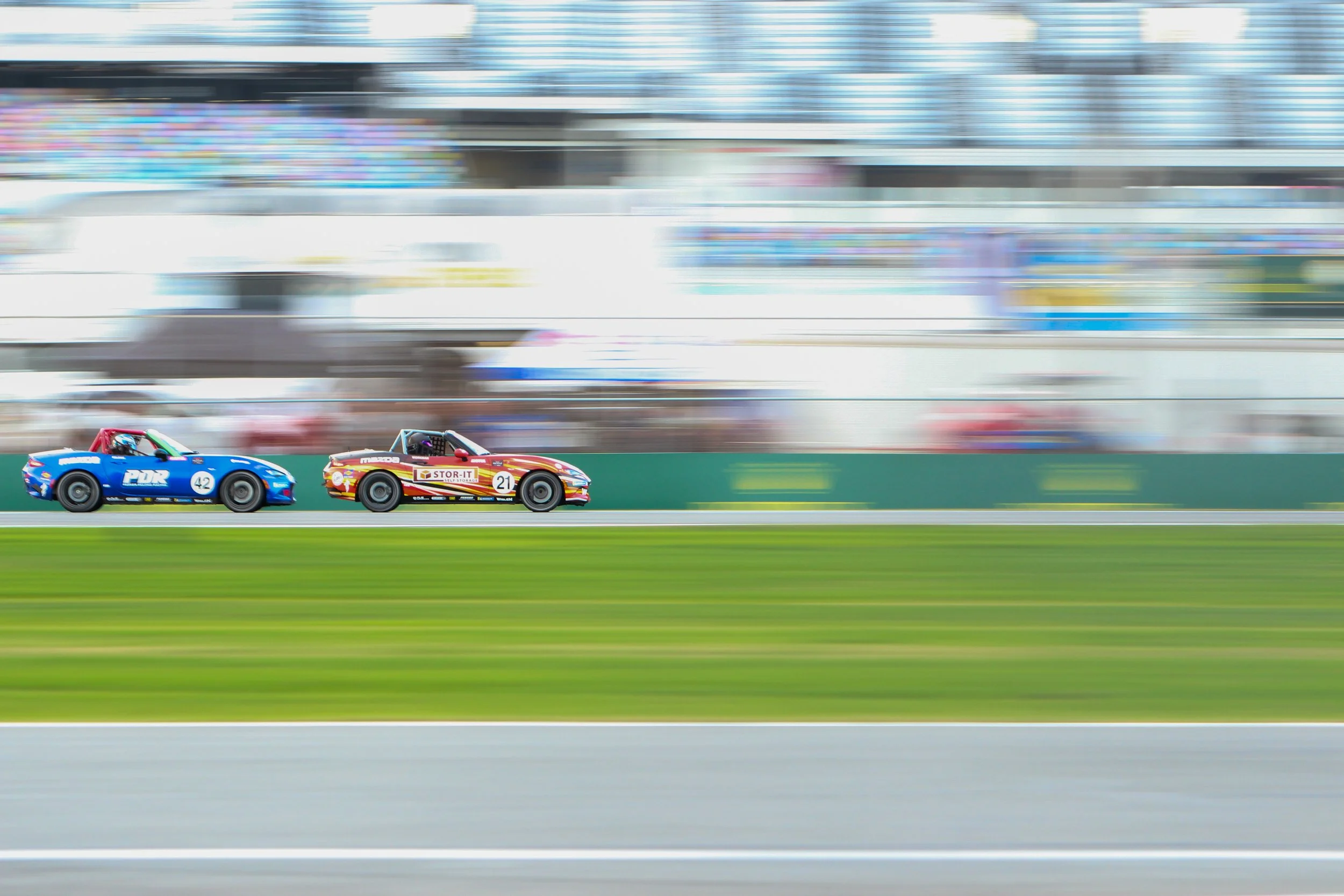 Two racing cars, one blue with number 42 and one red with number 21, racing on a track with blurred background.