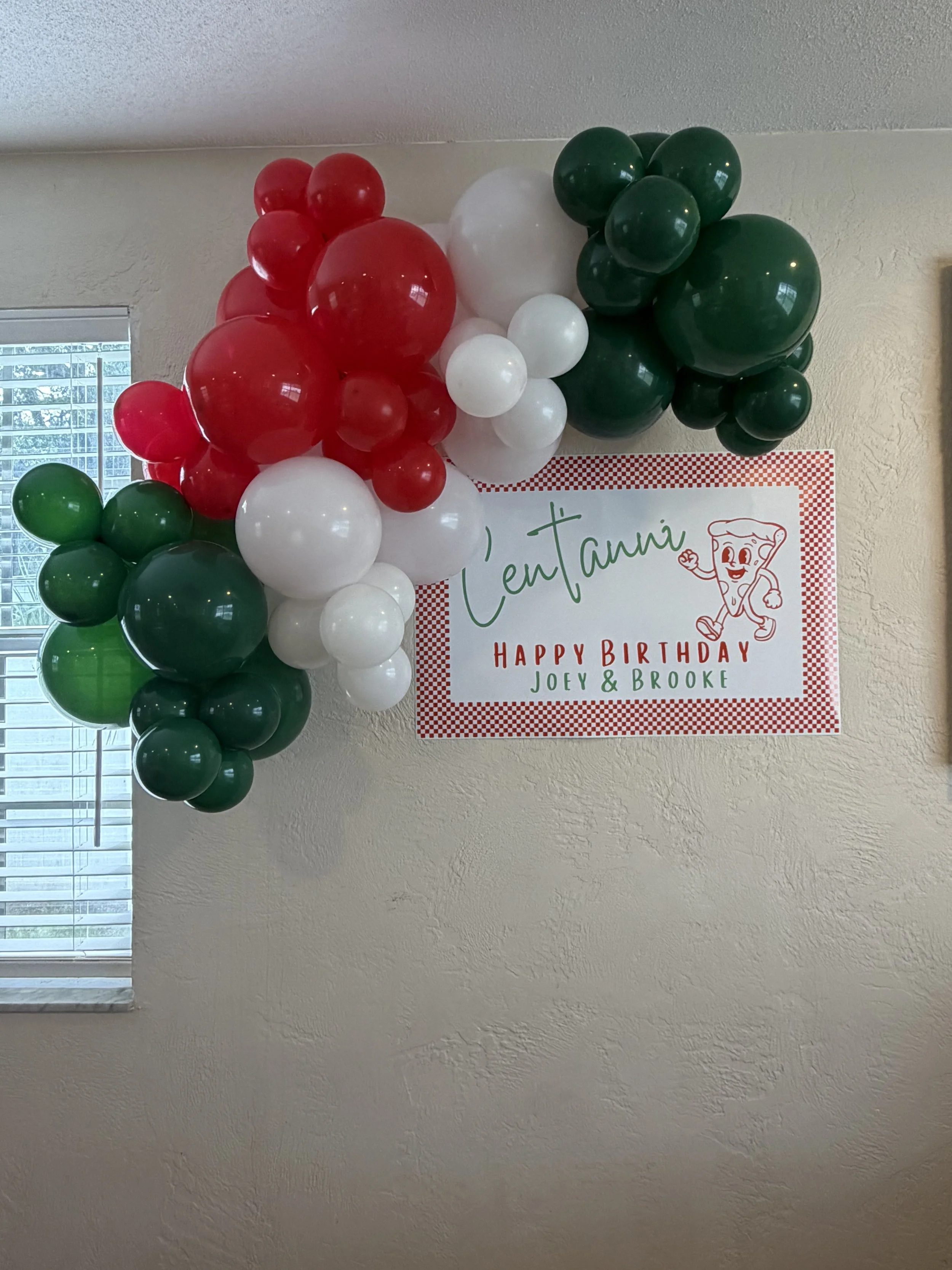 Decorative balloon arrangement in red, white, and green balloons on a wall with a birthday sign.
