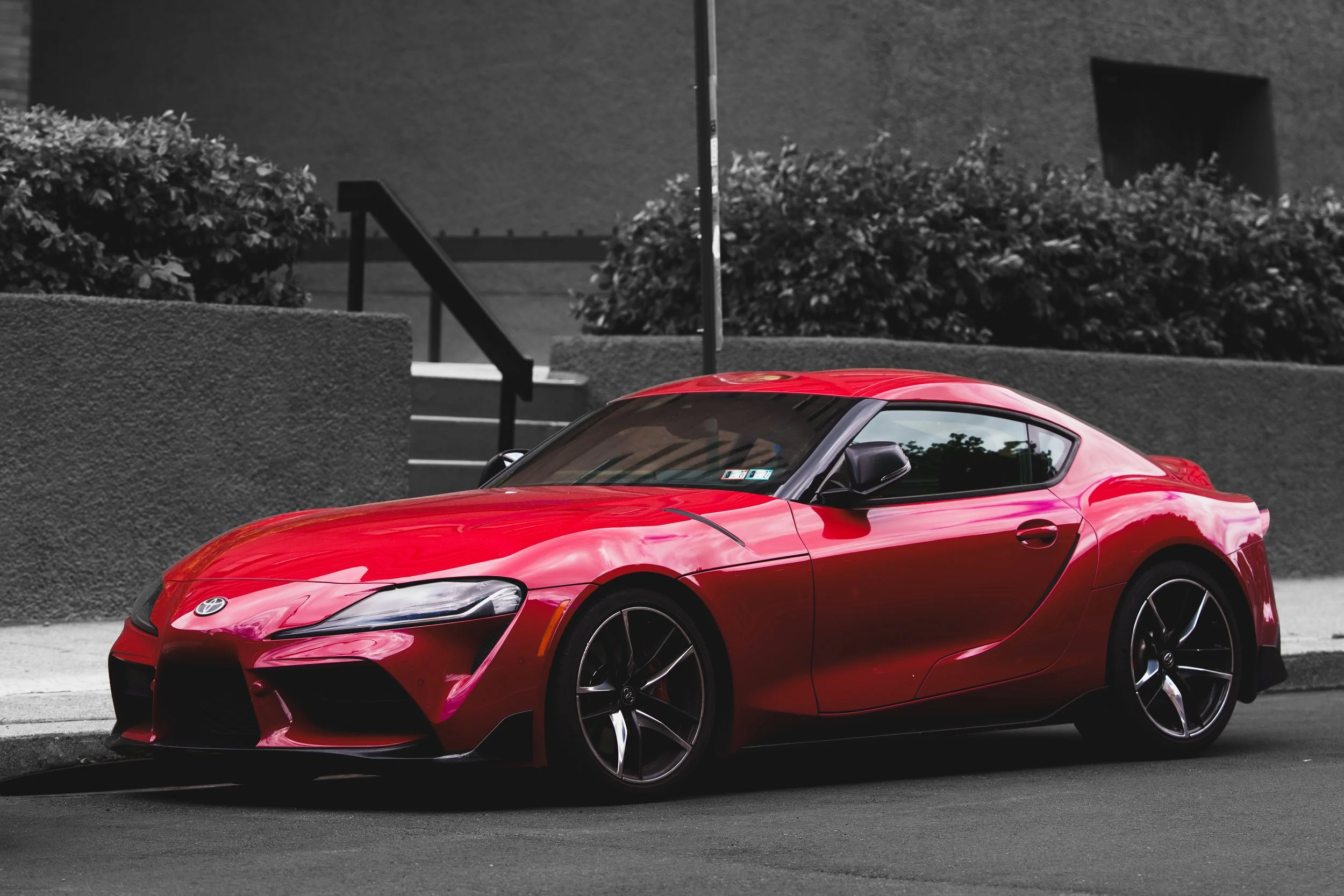 Red Toyota sports car parked on the street near stairs and bushes